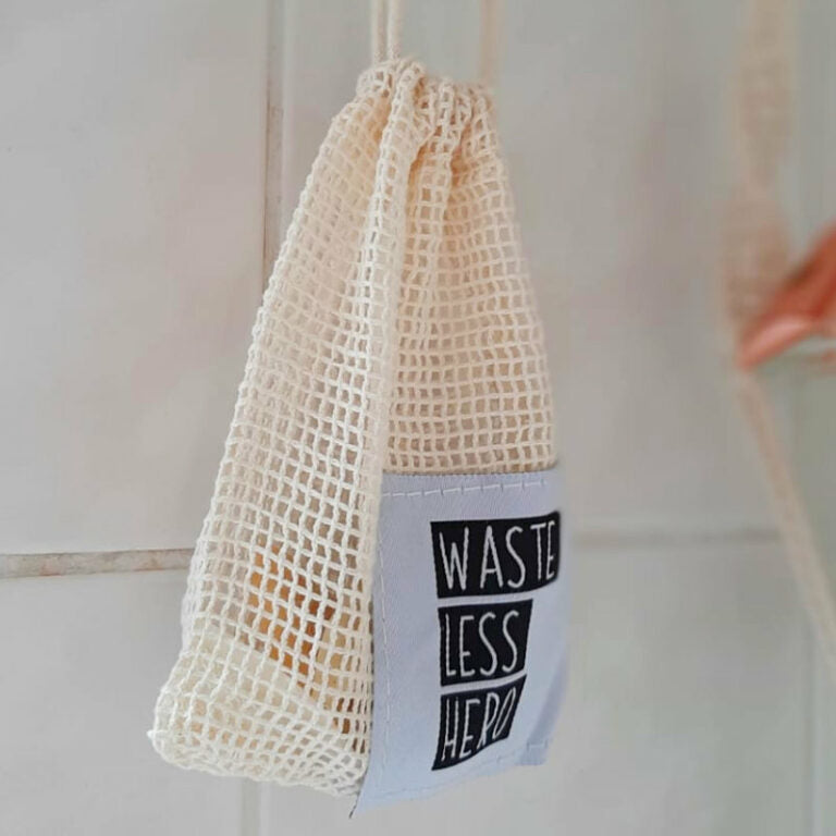 Ein beiger Netzbeutel mit dem Aufdruck "Waste Less Hero" hängt an einem Haken.