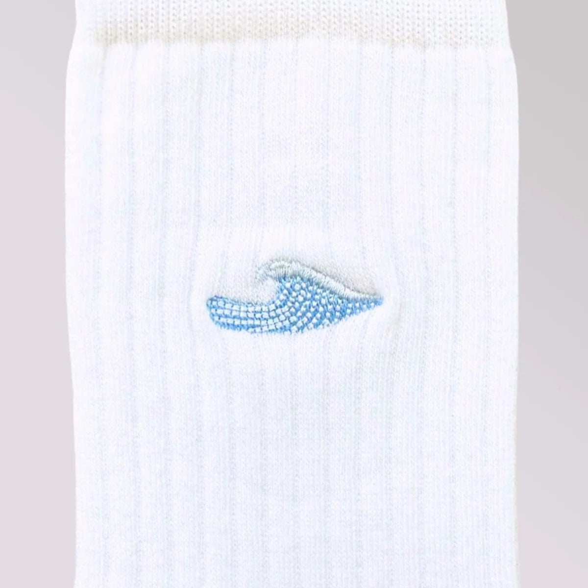 Nahaufnahme einer weißen gerippten Socke mit einem kleinen, aufgestickten blauen Wellenmuster am oberen Rand.