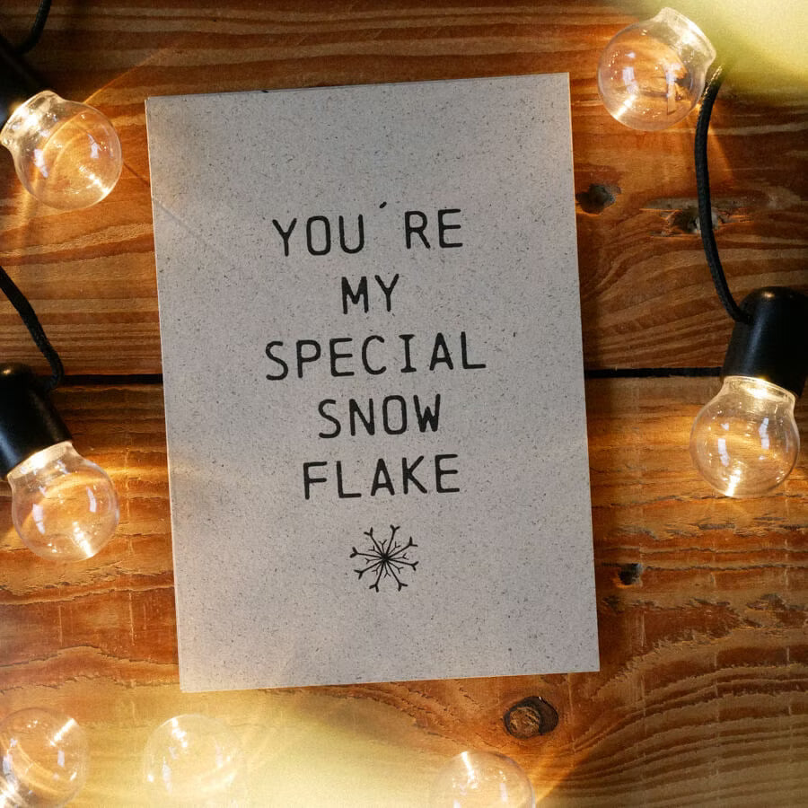 Karte mit der Aufschrift "YOU'RE MY SPECIAL SNOWFLAKE" auf einem Holztisch, umrahmt von Lichterketten.