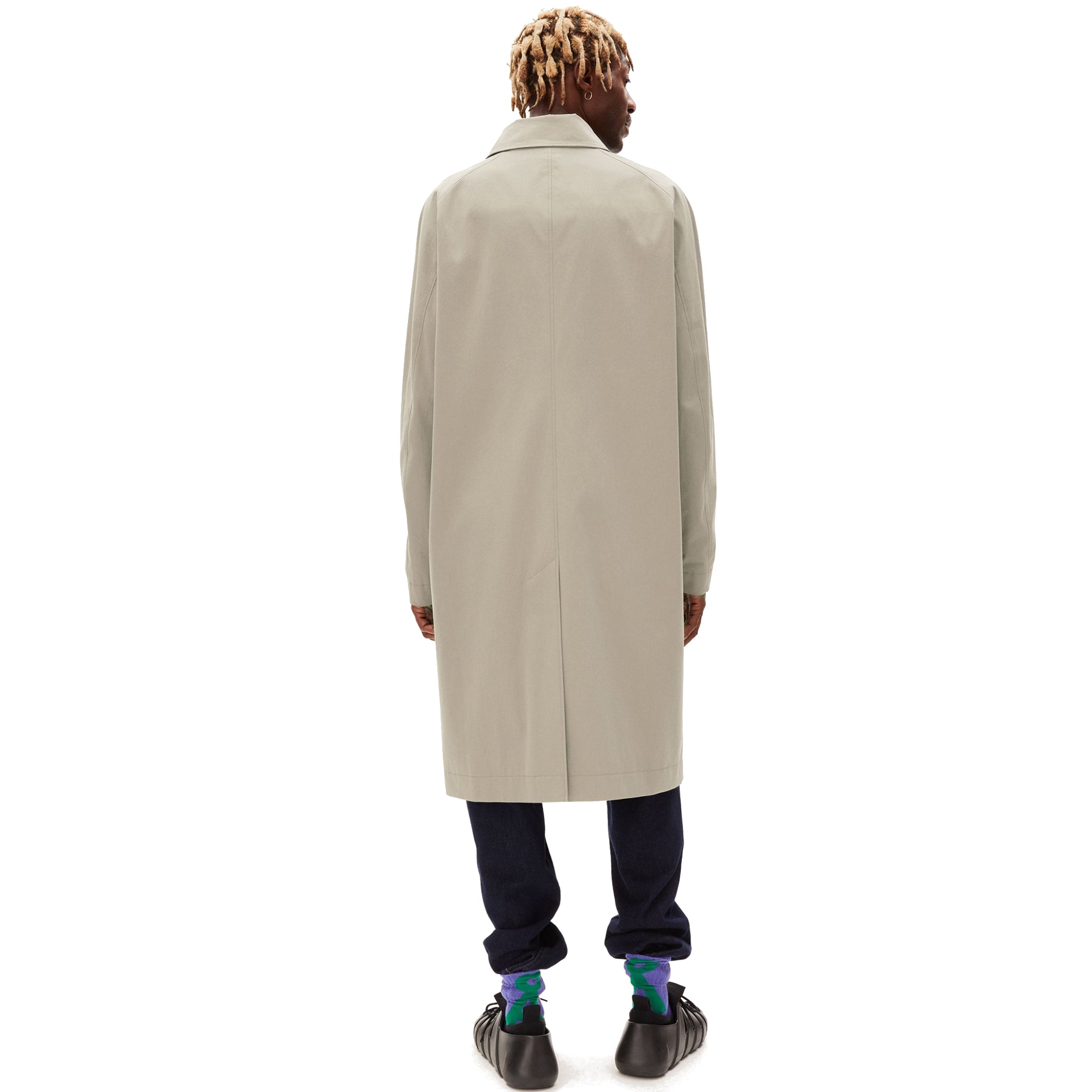 Person von hinten in beigem Mantel, dunkler Hose und bunten Socken.