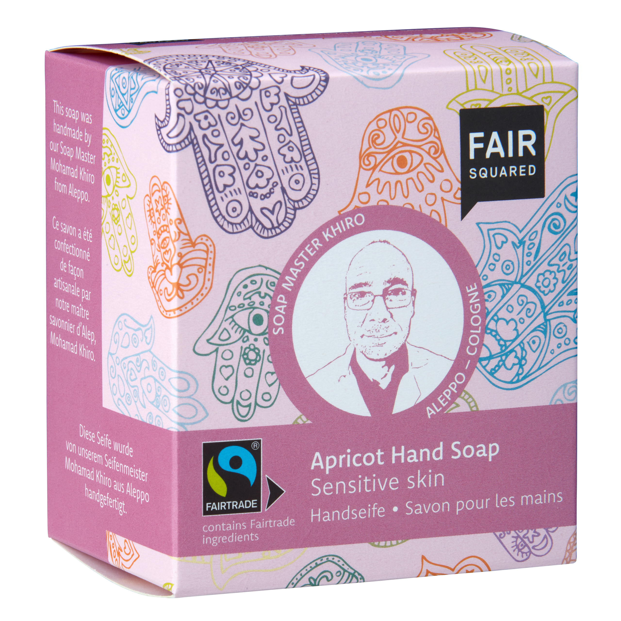 Eine rosafarbene Schachtel der Fair Squared Aprikosen-Handseife für empfindliche Haut mit bunten Hamsa-Handmotiven, einem Porträt des Seifenmeisters Khiro und der Fairtrade-Zertifizierung auf der Vorderseite.