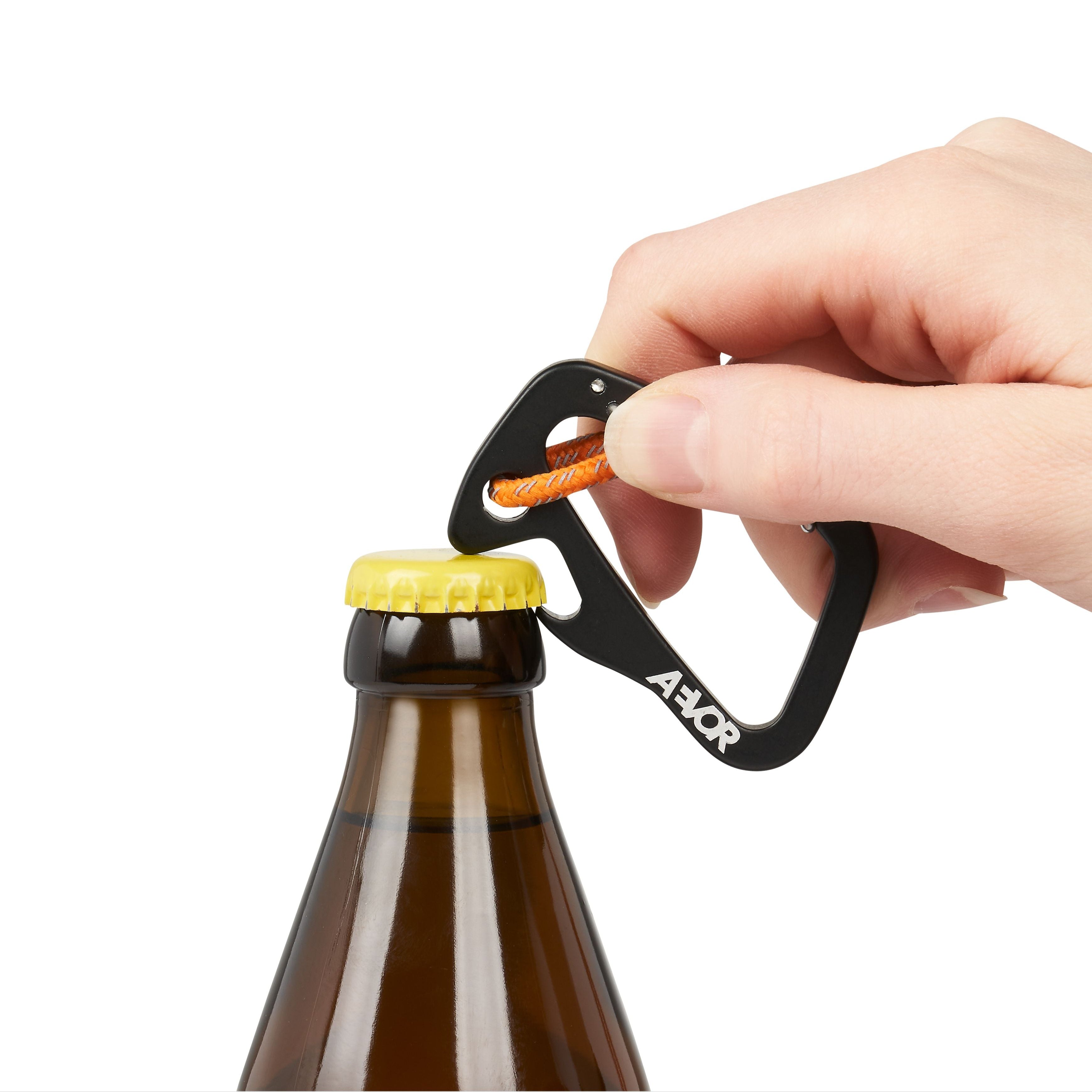 Eine Hand benutzt einen schwarzen Karabiner mit einem orangefarbenen Seil, um eine verschlossene braune Glasflasche zu öffnen. Der Hintergrund ist einfarbig weiß.