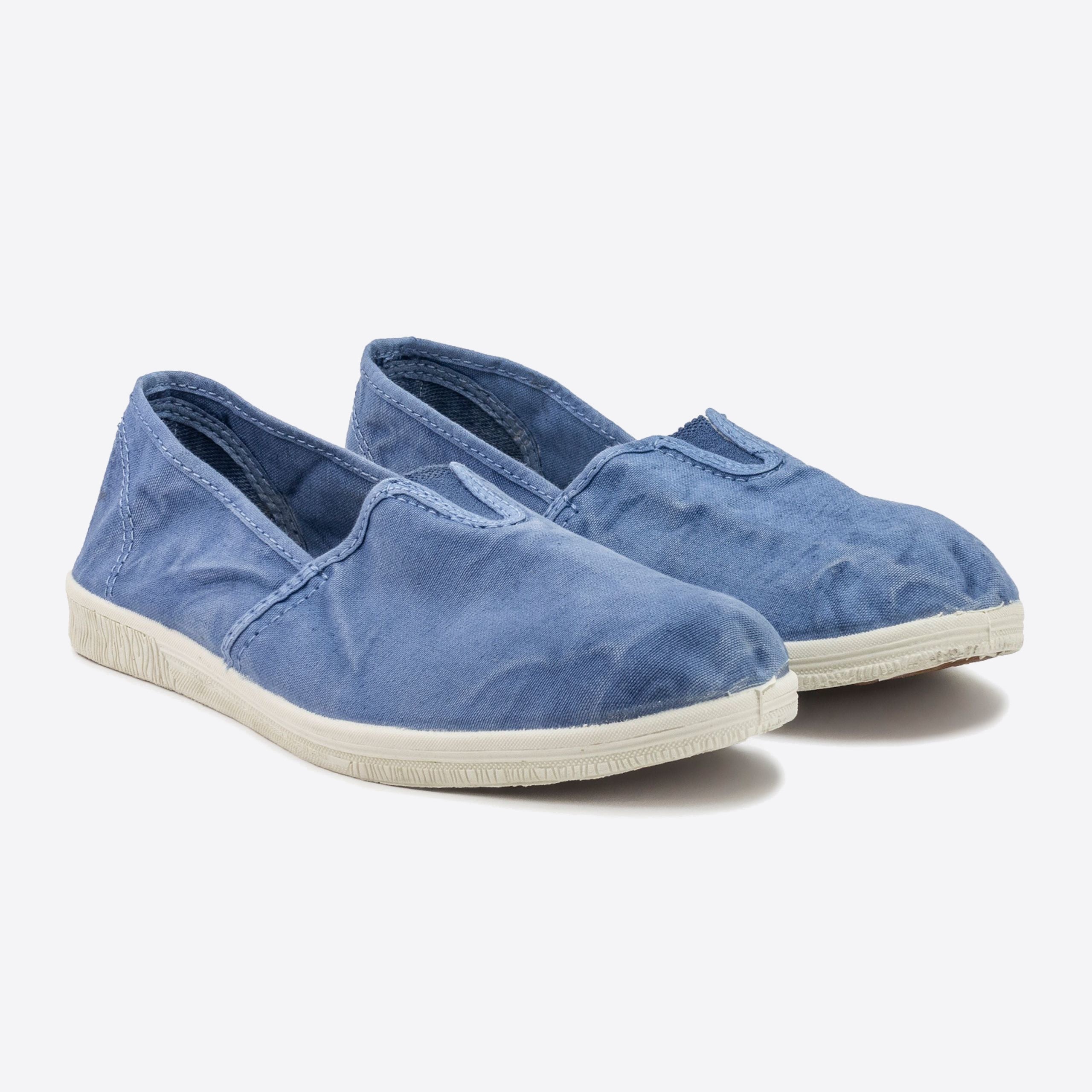 Blaue Leinenschuhe mit weißen Sohlen, von schräg oben fotografiert, auf weißem Hintergrund.