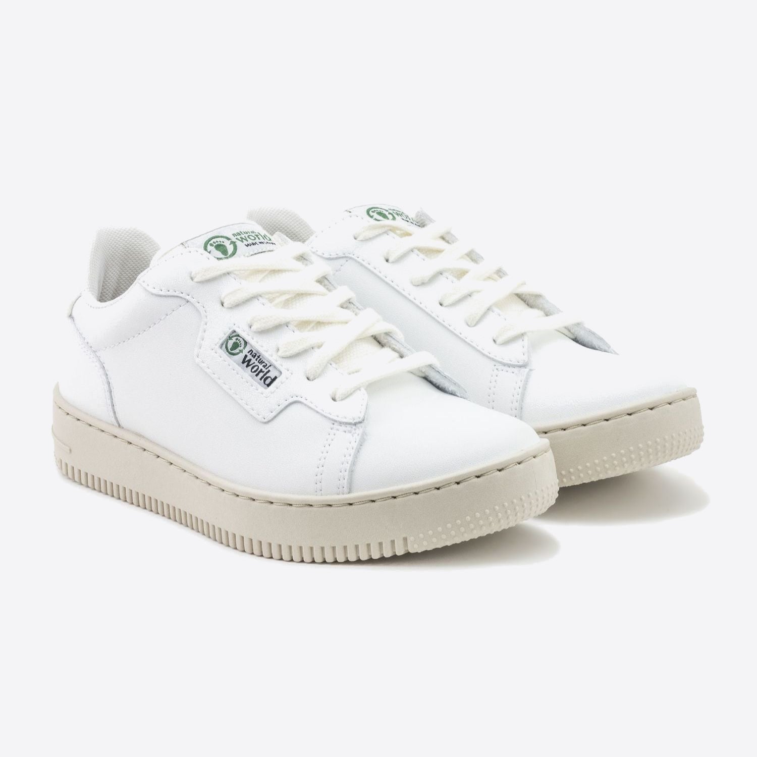 Weiße Sneaker mit beigen Sohlen und grünen Logos auf der Zunge und Seite, präsentiert auf hellem Hintergrund.