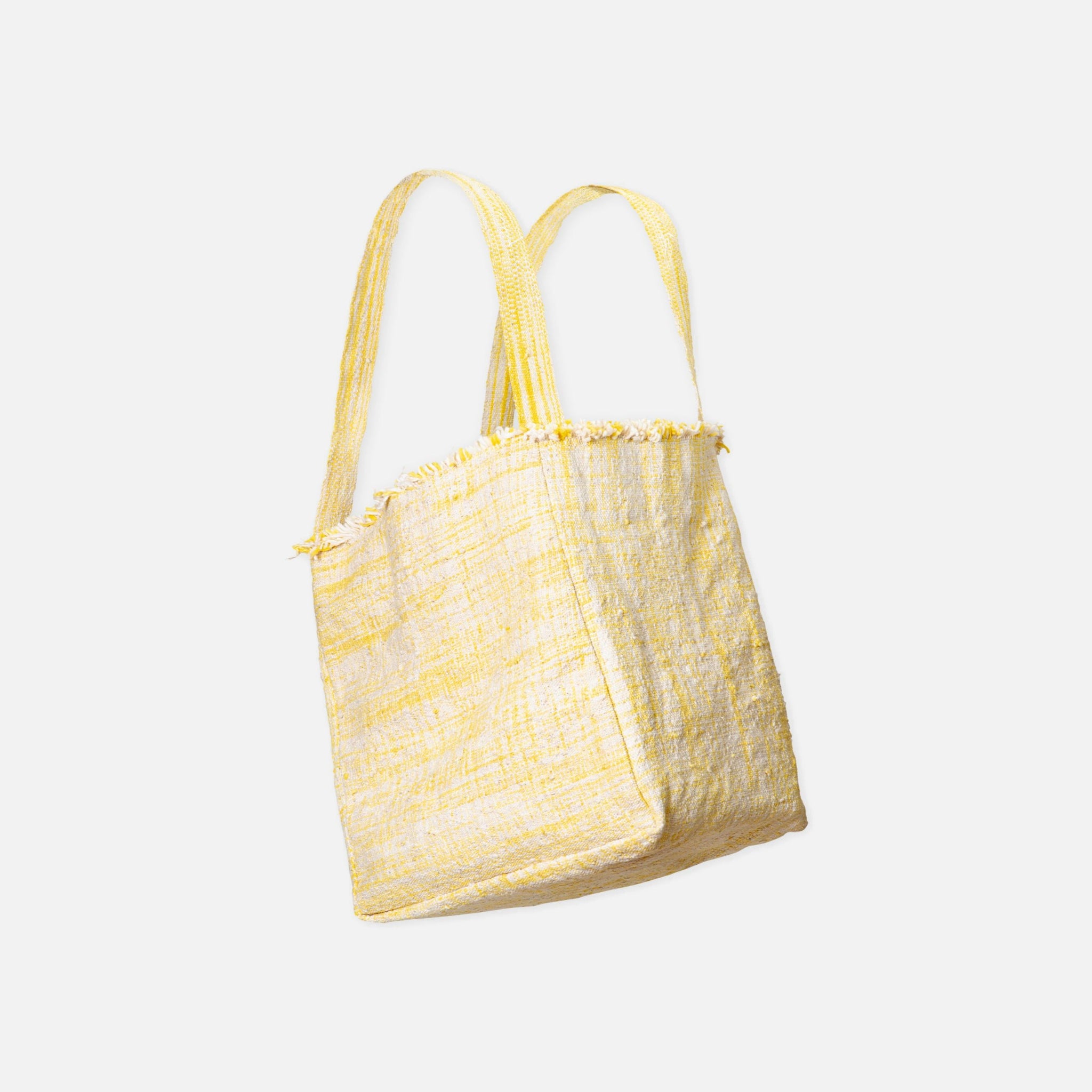 Gelbe Stofftasche mit Fransen an der Oberkante und langen Trägern vor weißem Hintergrund.