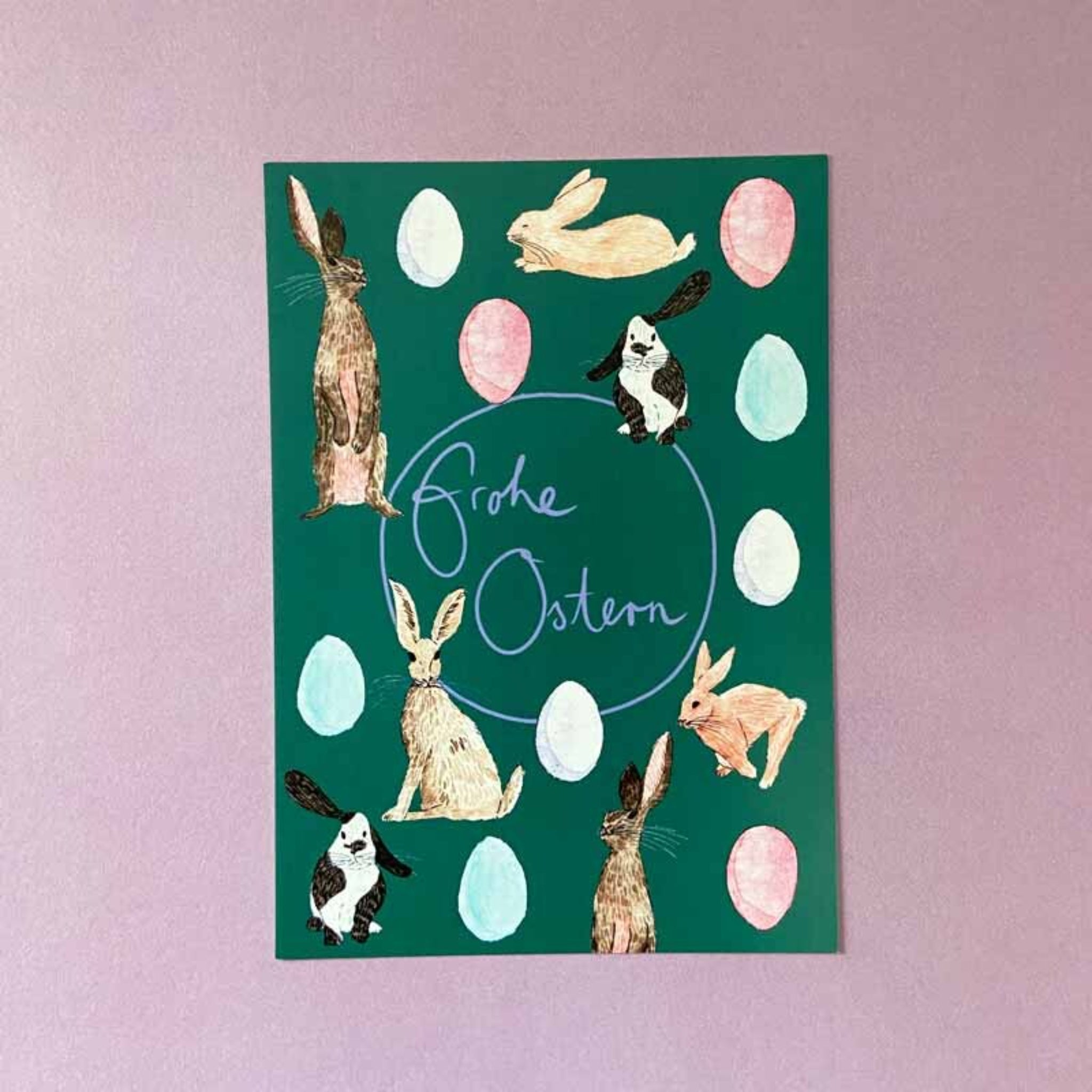 Grüne Osterkarte mit gezeichneten Hasen und Eiern sowie dem Schriftzug "Frohe Ostern" auf lila Hintergrund.