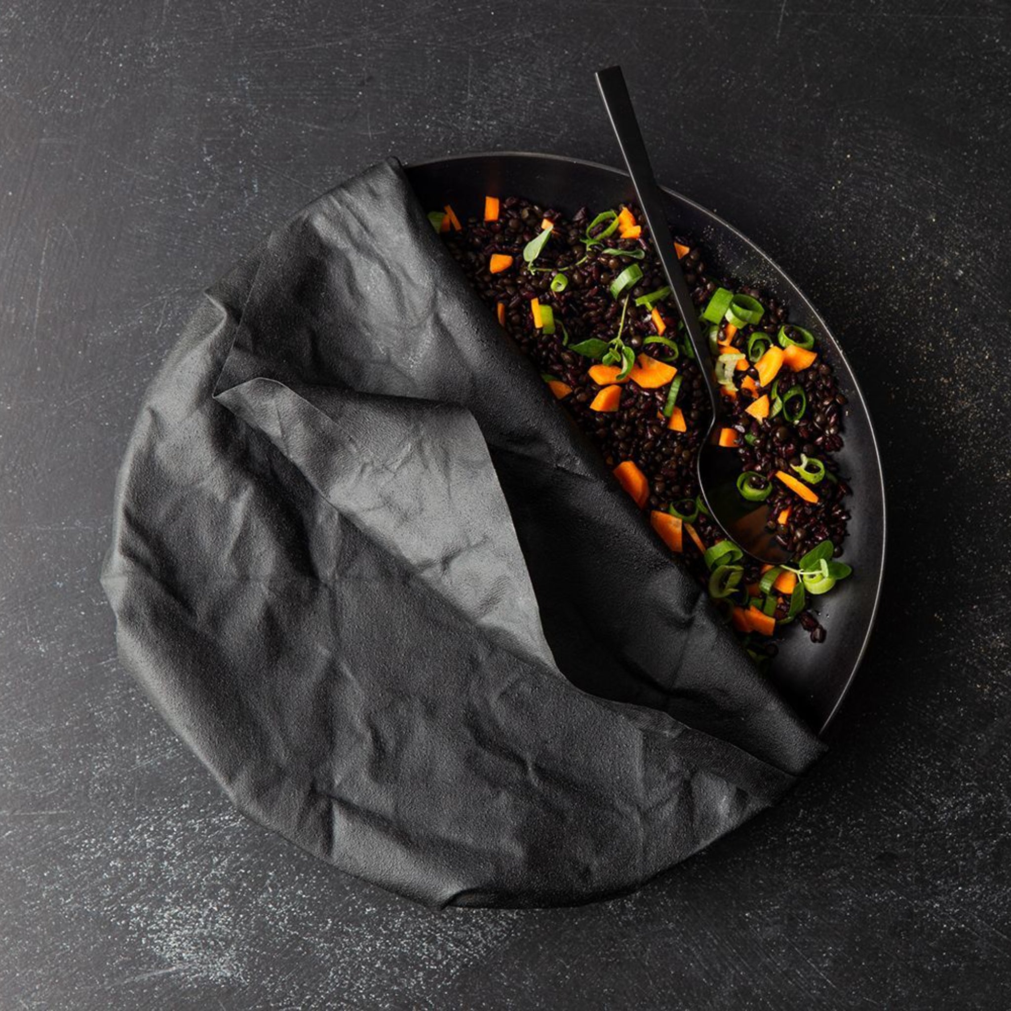 Schwarze Schale mit Linsensalat, Karottenstücken und Frühlingszwiebeln, teilweise bedeckt mit einem dunklen Tuch.