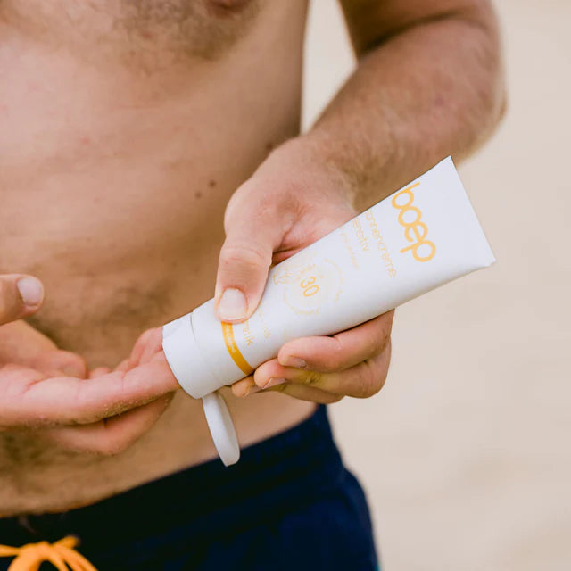 Eine Person trägt Sonnencreme mit Lichtschutzfaktor 30 auf, während sie am Strand steht.