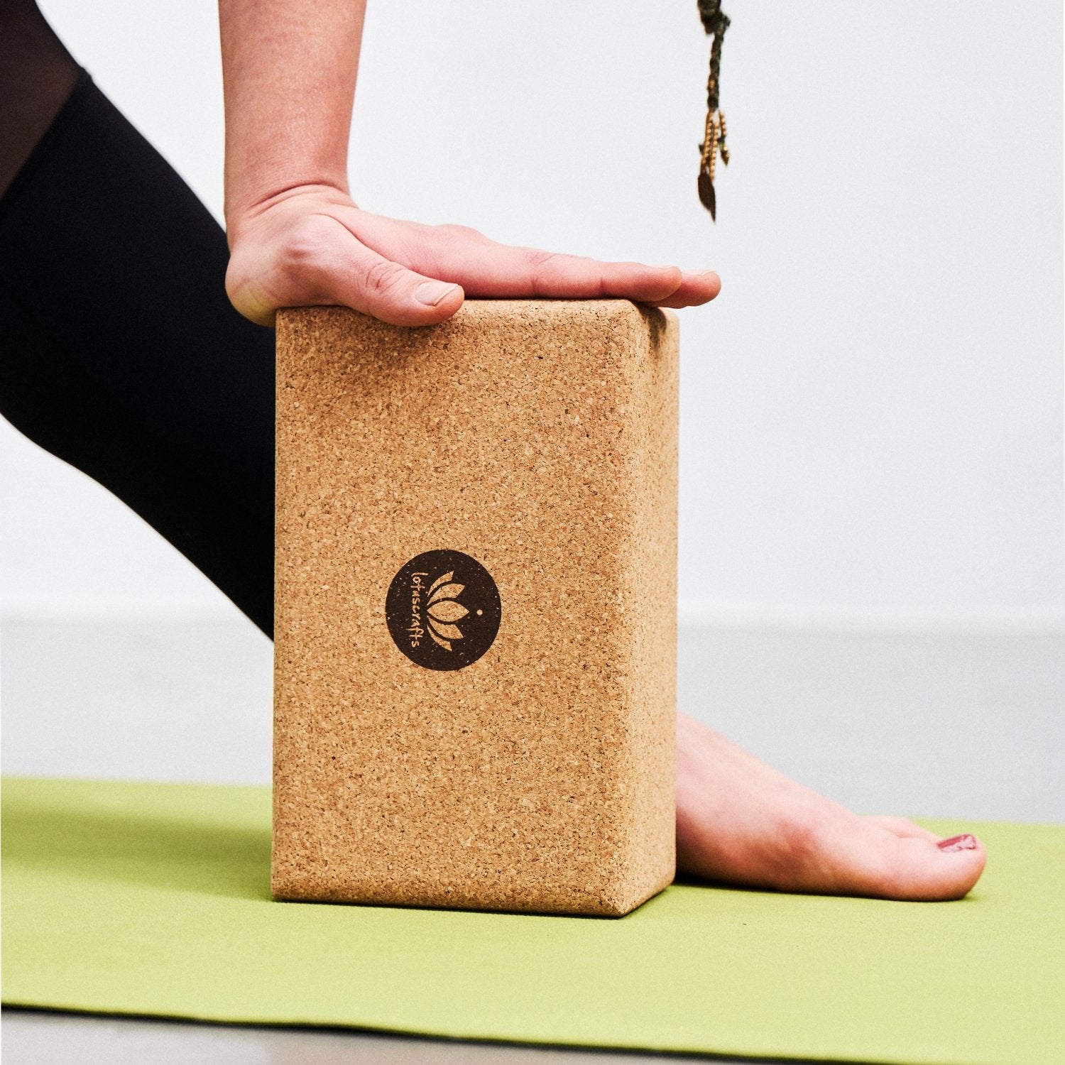 Ein Yoga-Block aus Kork auf einer grünen Matte, von einer Hand stabilisiert und einem nackten Fuß unterstützt.