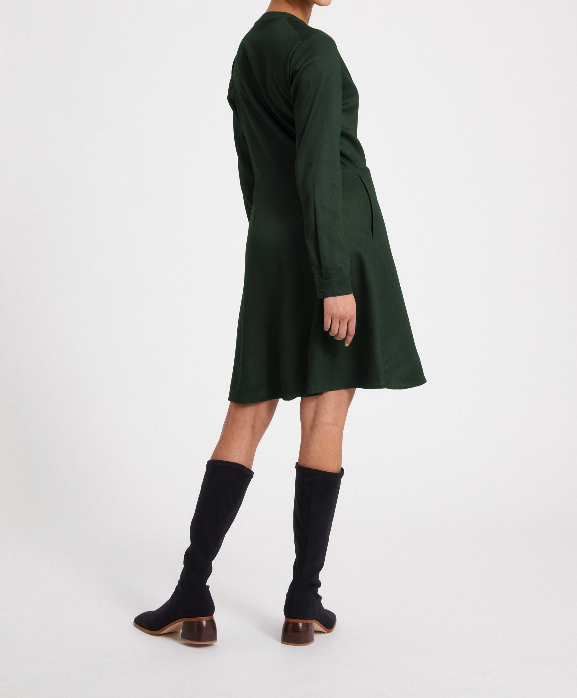 Person in green dress and black knee-high boots poses against a white background.