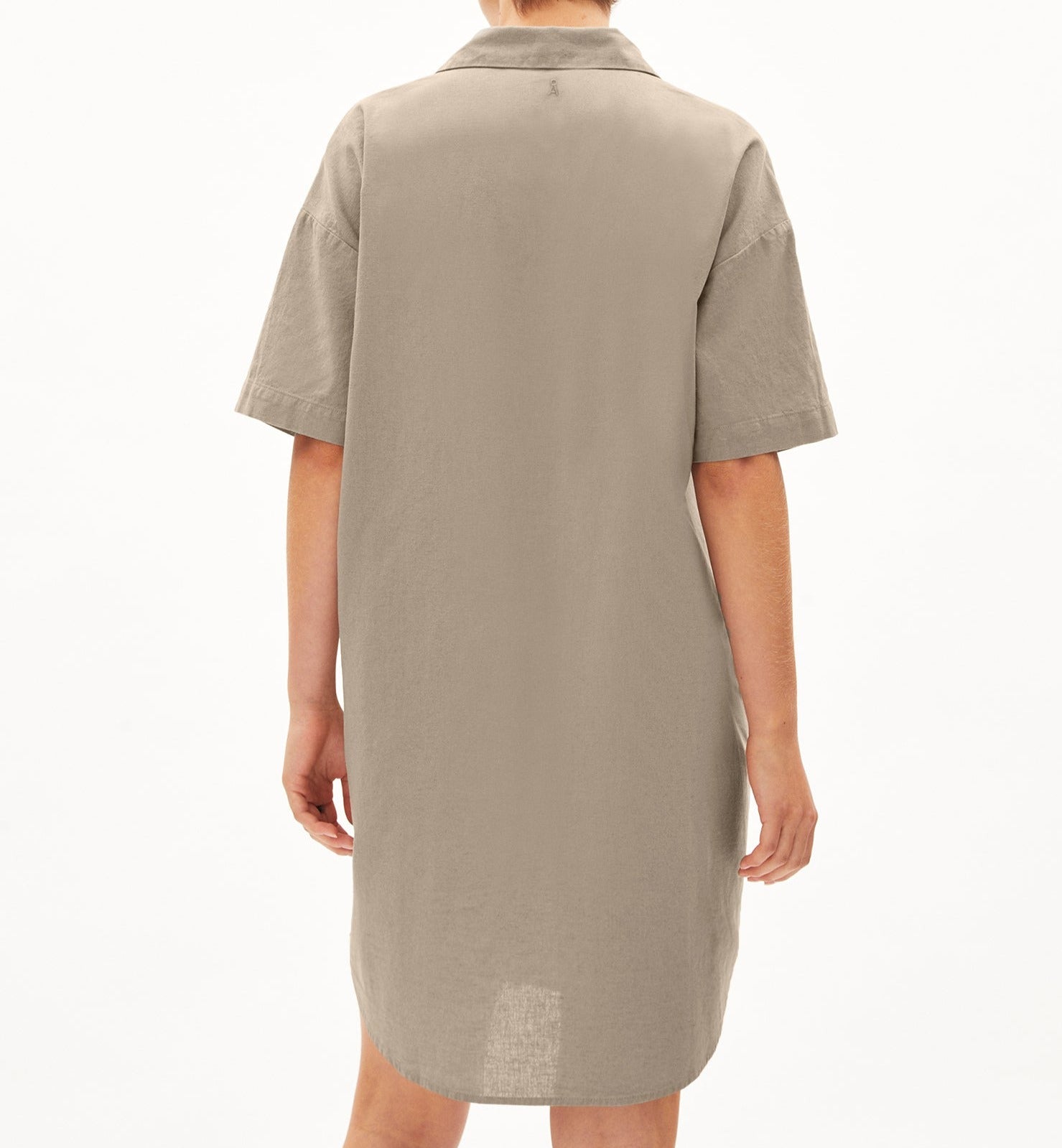 Eine Person trägt ein beiges Hemdkleid, gezeigt von hinten mit kurzen Ärmeln und einem Kragen, vor einem weißen Hintergrund.