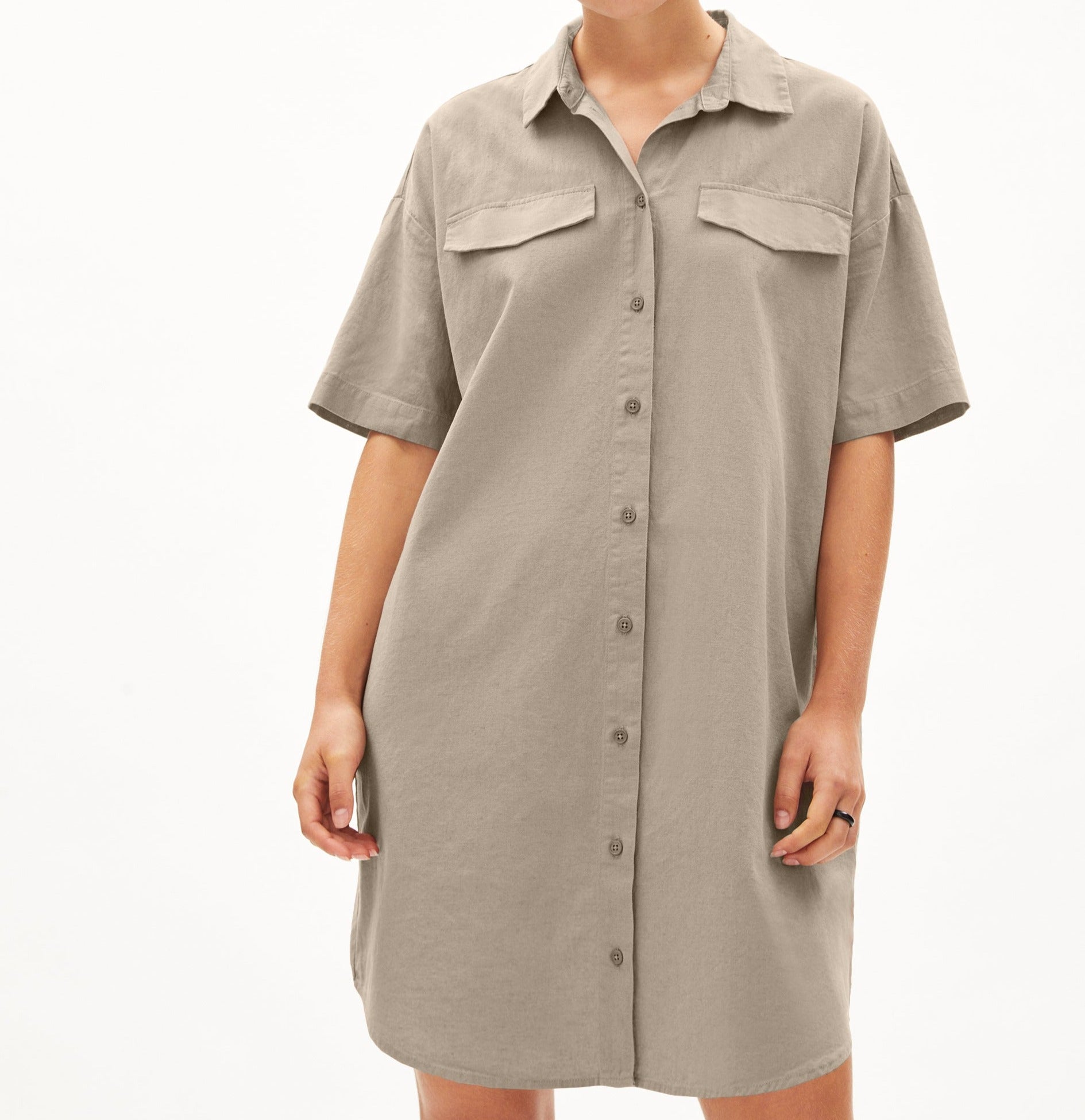 Eine Person trägt ein locker sitzendes, beigefarbenes Hemdkleid mit kurzen Ärmeln und durchgehender Knopfleiste.