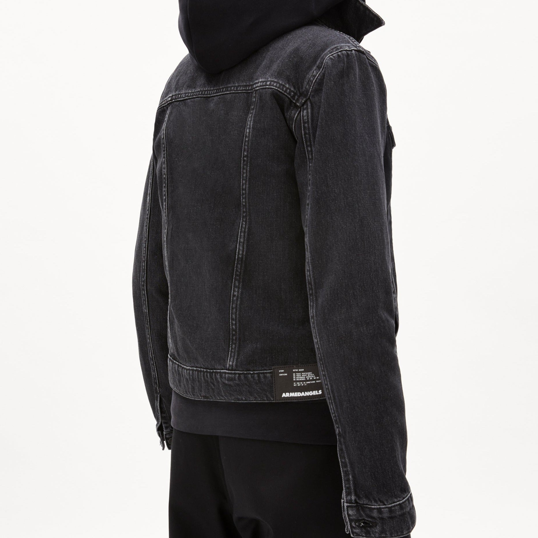 Person in schwarzer Denimjacke von hinten, mit Kapuzenpullover darunter vor weißem Hintergrund.