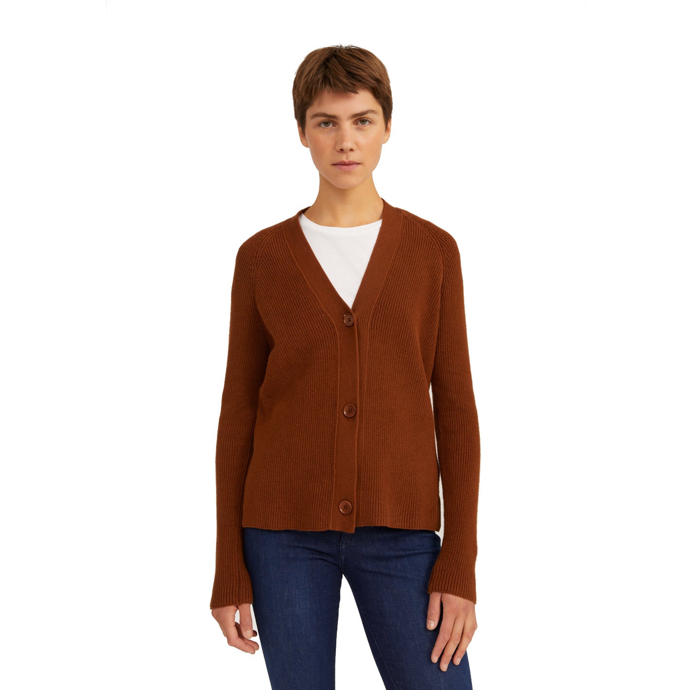 Person in brauner Strickjacke mit Knöpfen und blauer Jeans vor weißem Hintergrund.