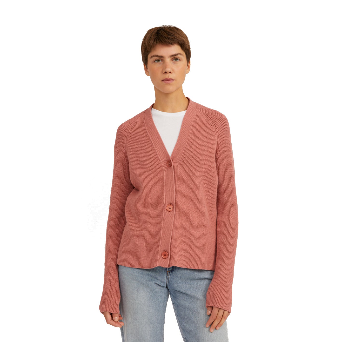 Person in rosa Strickjacke mit Knöpfen und blauer Jeans steht vor weißem Hintergrund.