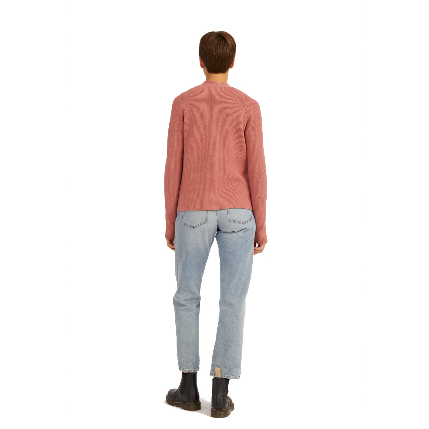 Person von hinten in rosa Pullover, blauen Jeans und schwarzen Stiefeln vor weißem Hintergrund.