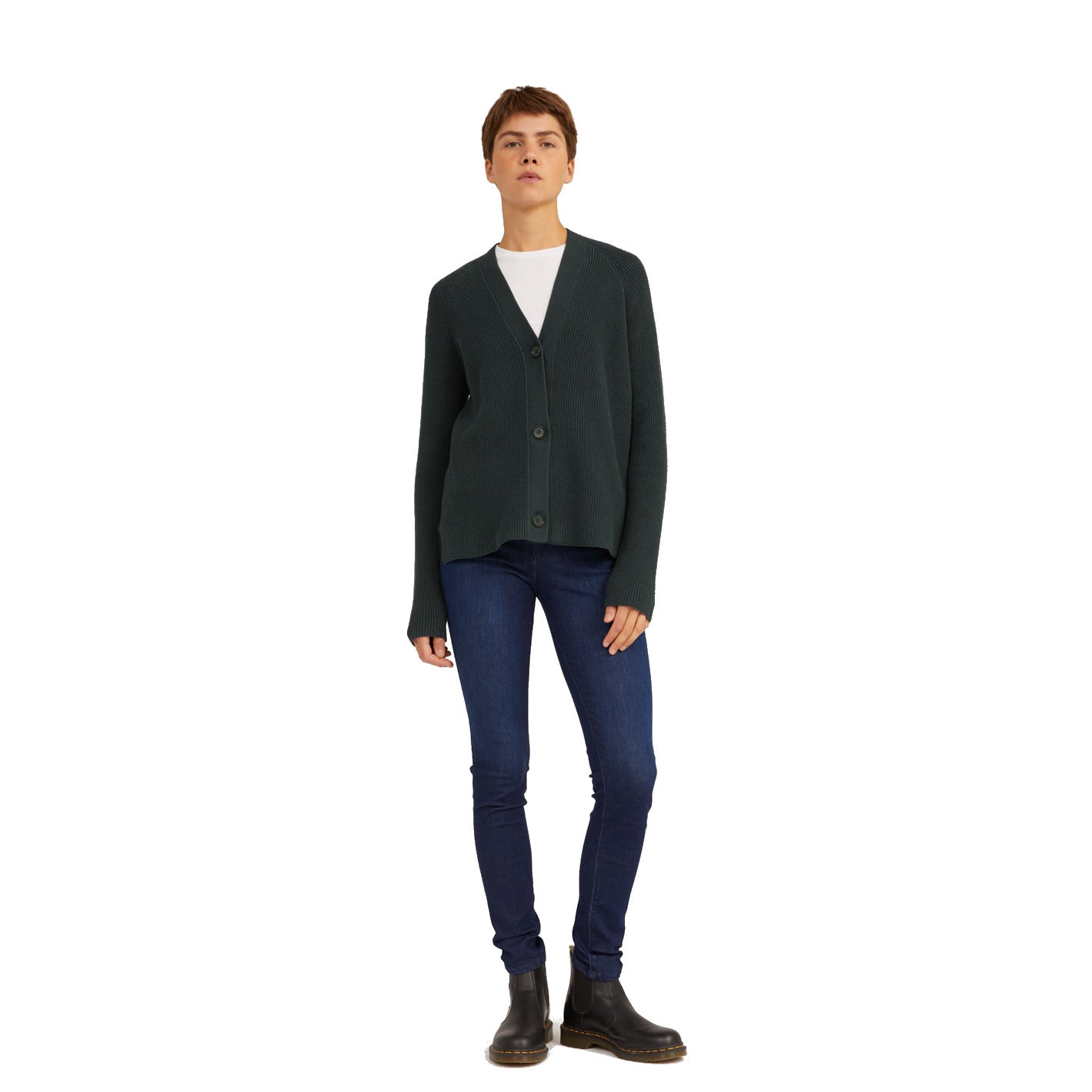 Person in dunkelblauer Strickjacke, weißem T-Shirt, blauer Jeans und schwarzen Chelsea-Boots steht vor weißem Hintergrund.