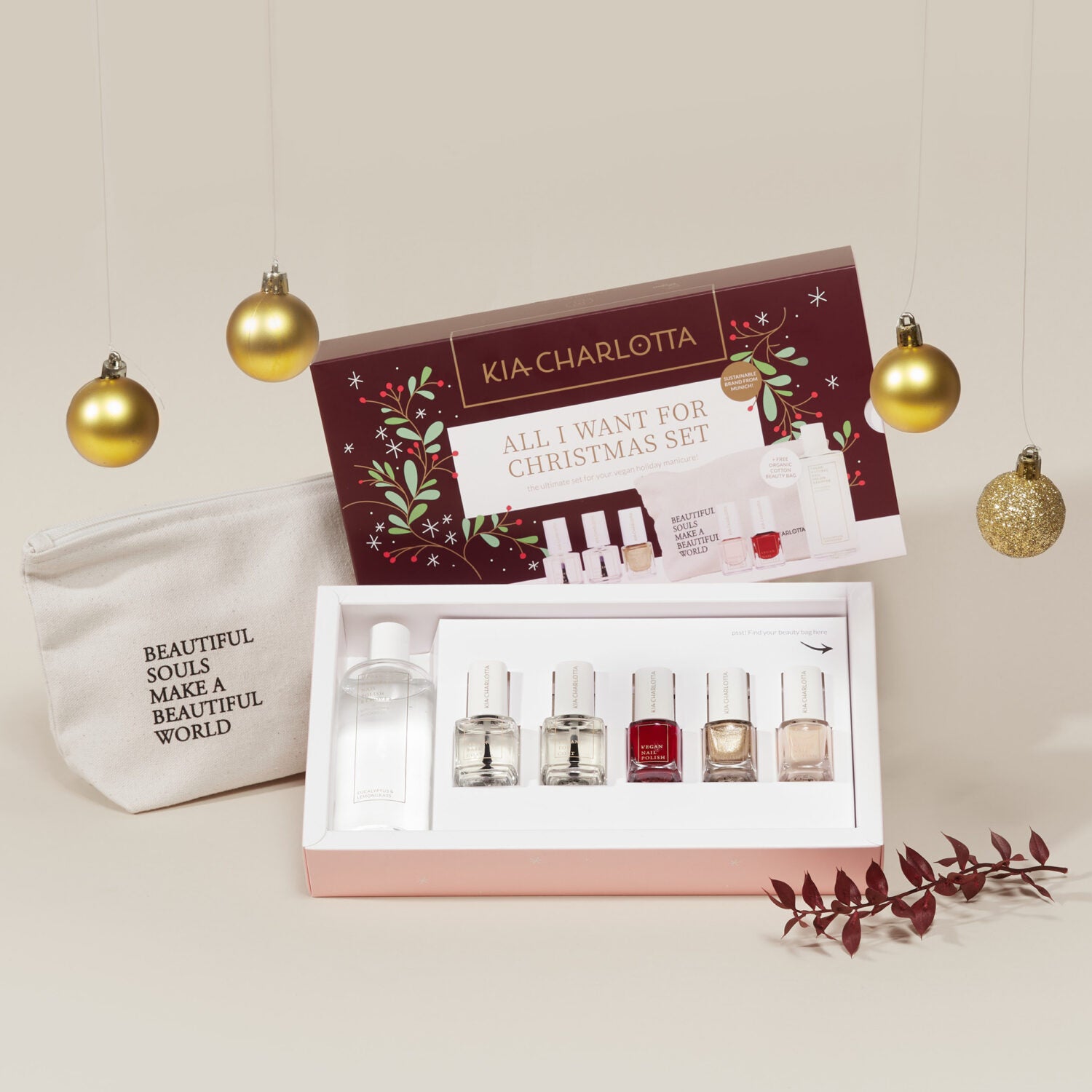 Weihnachtsset mit Nagellacken und einer Flasche, umgeben von goldenen Kugeln, neben einer Tasche mit Schriftzug.