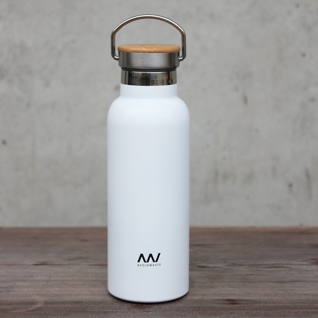 Weiße Wasserflasche mit Holzdeckel und Metallgriff auf einem Holztisch vor grauem Hintergrund.