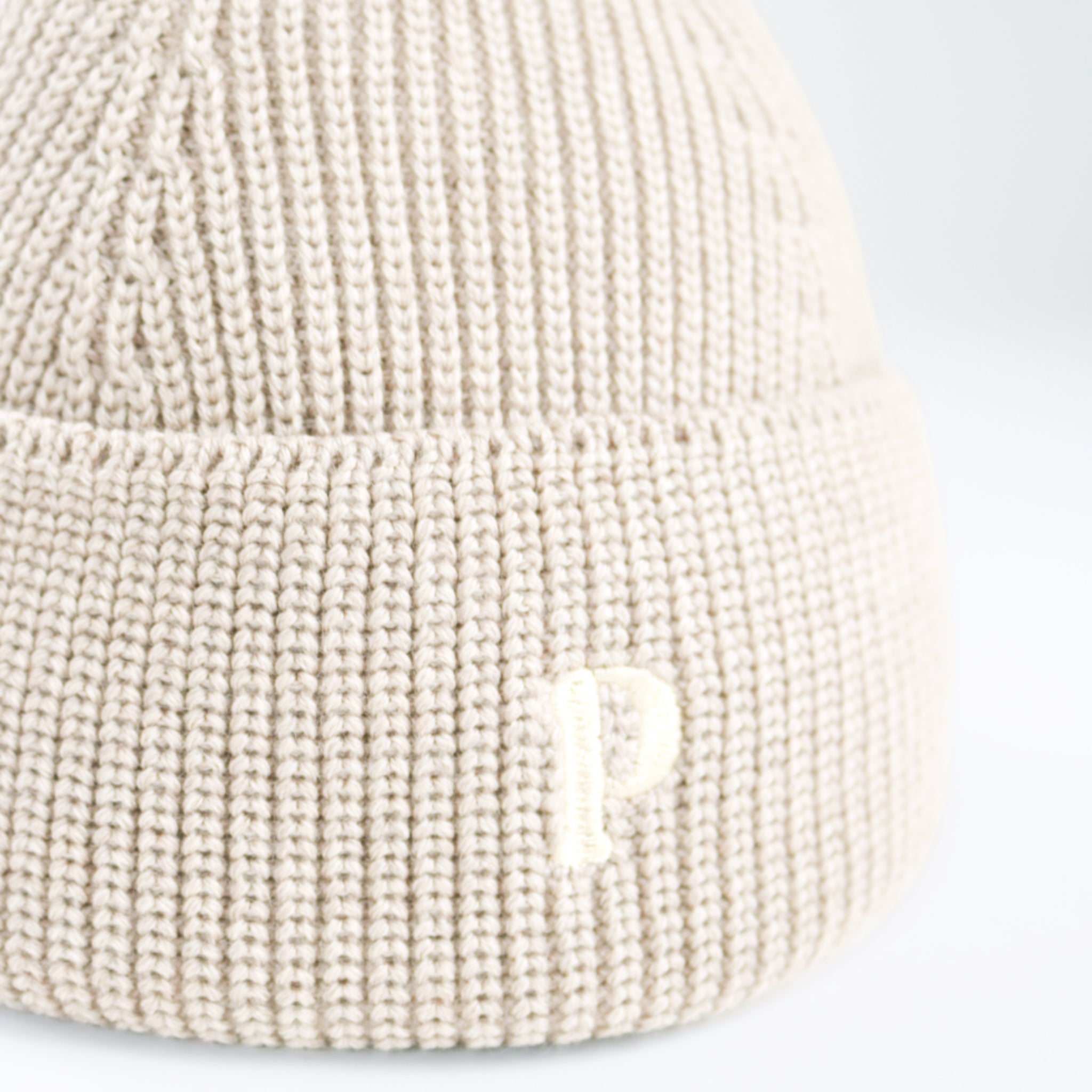 Nahaufnahme einer beigefarbenen Strickmütze mit einem eingestickten Buchstaben "P".