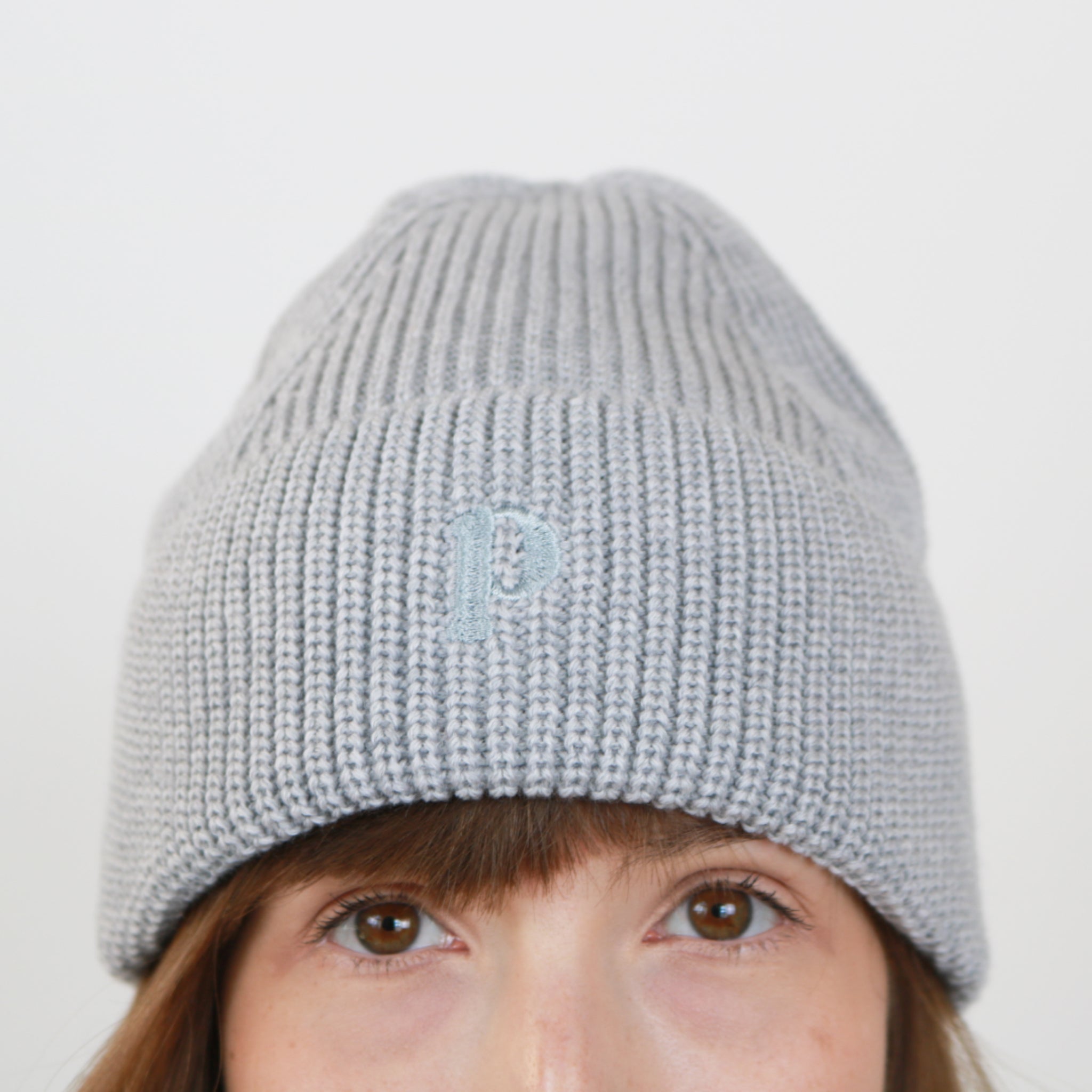 Person mit grauer Strickmütze, auf der ein kleines "p" eingestickt ist.