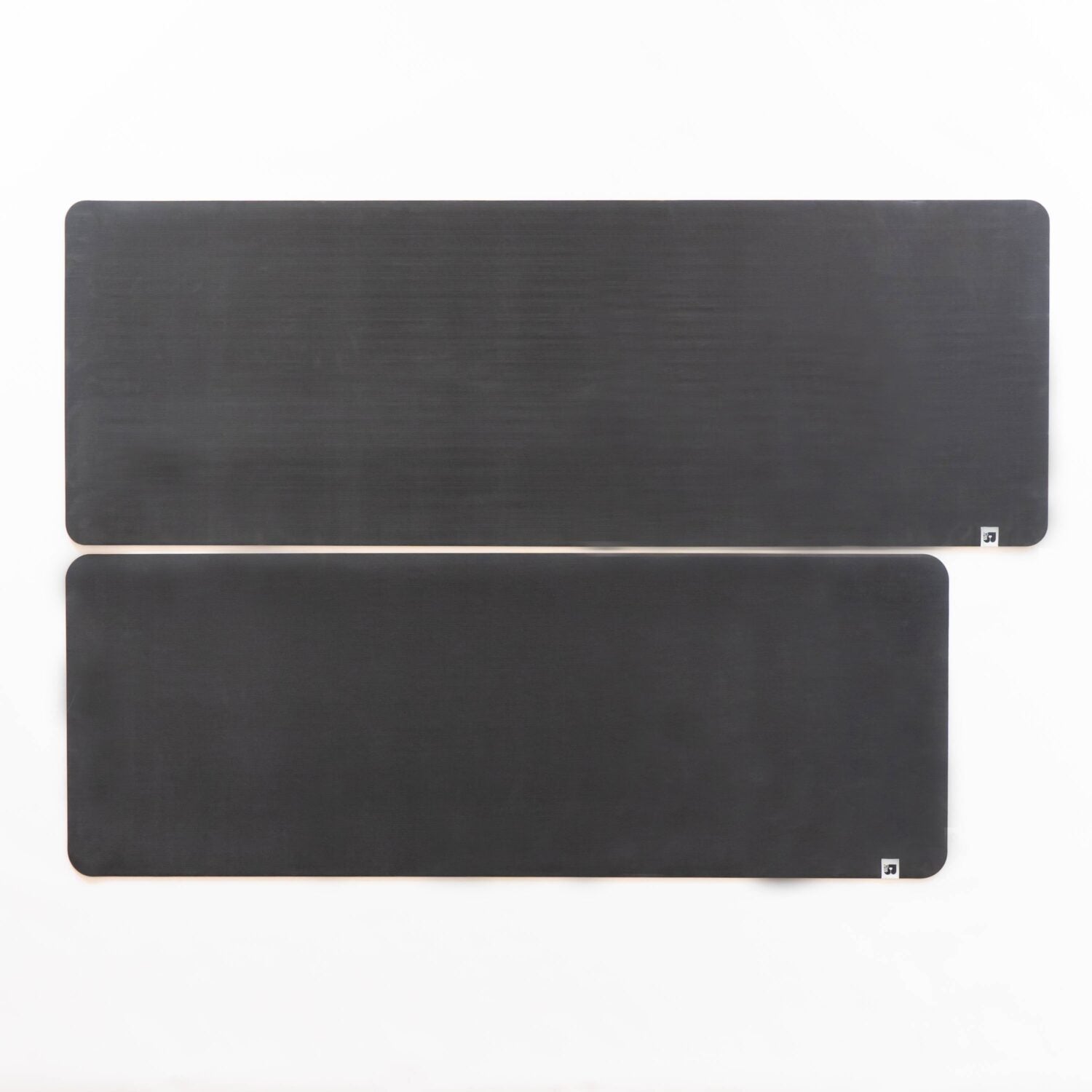 Zwei schwarze, rechteckige Matten mit abgerundeten Ecken, nebeneinander auf einem weißen Hintergrund.