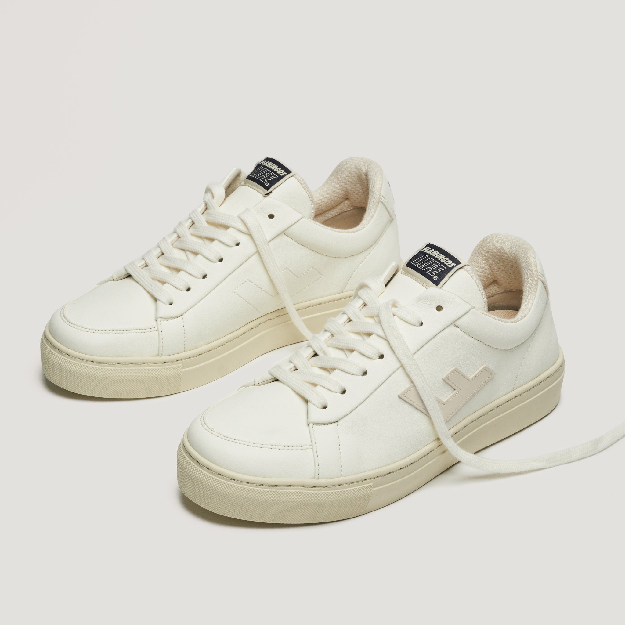 Weiße Turnschuhe auf hellem Hintergrund mit beigen Sohlen und schwarzen Labels auf den Zungen.