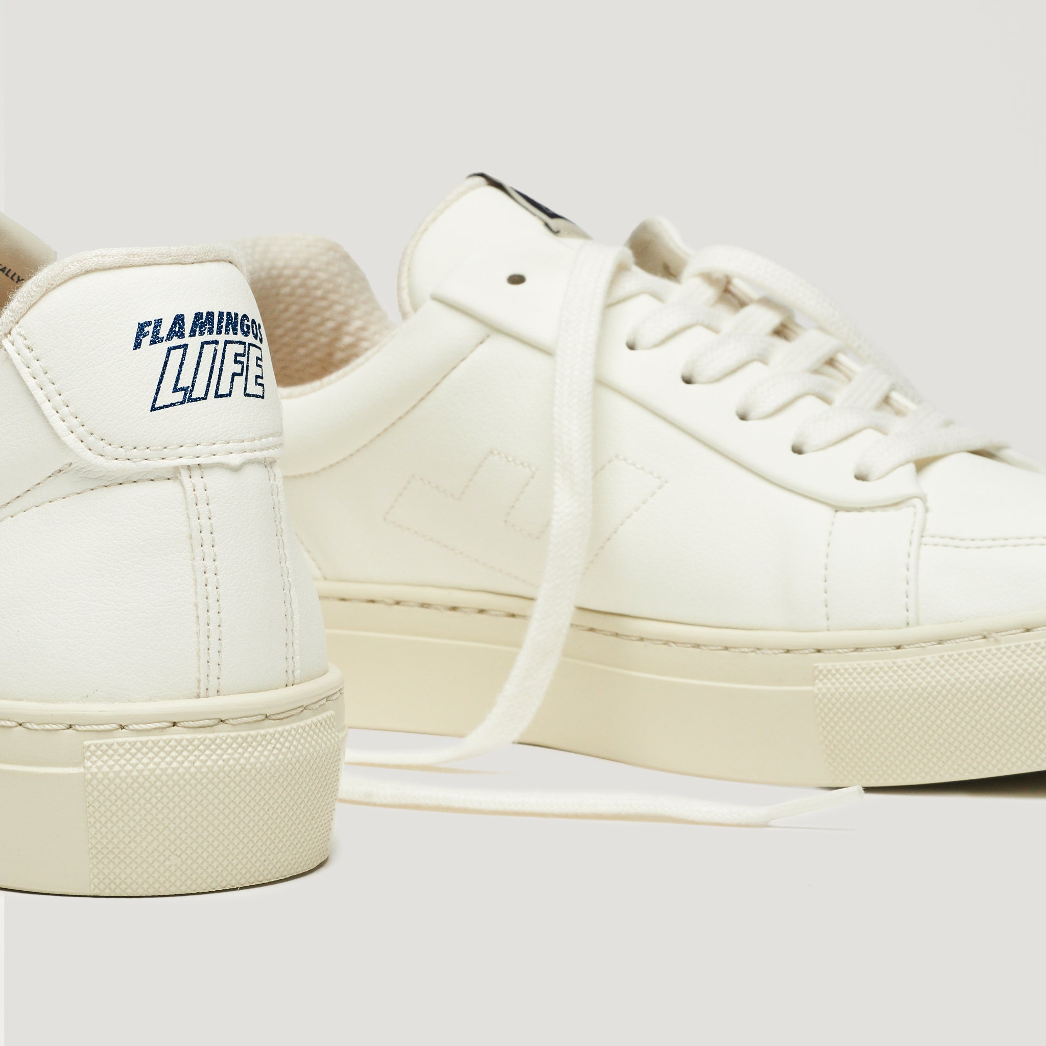 Weiße Sneakers mit blauem "FLAMINGO'S LIFE"-Schriftzug auf der Ferse und weißen Schnürsenkeln.