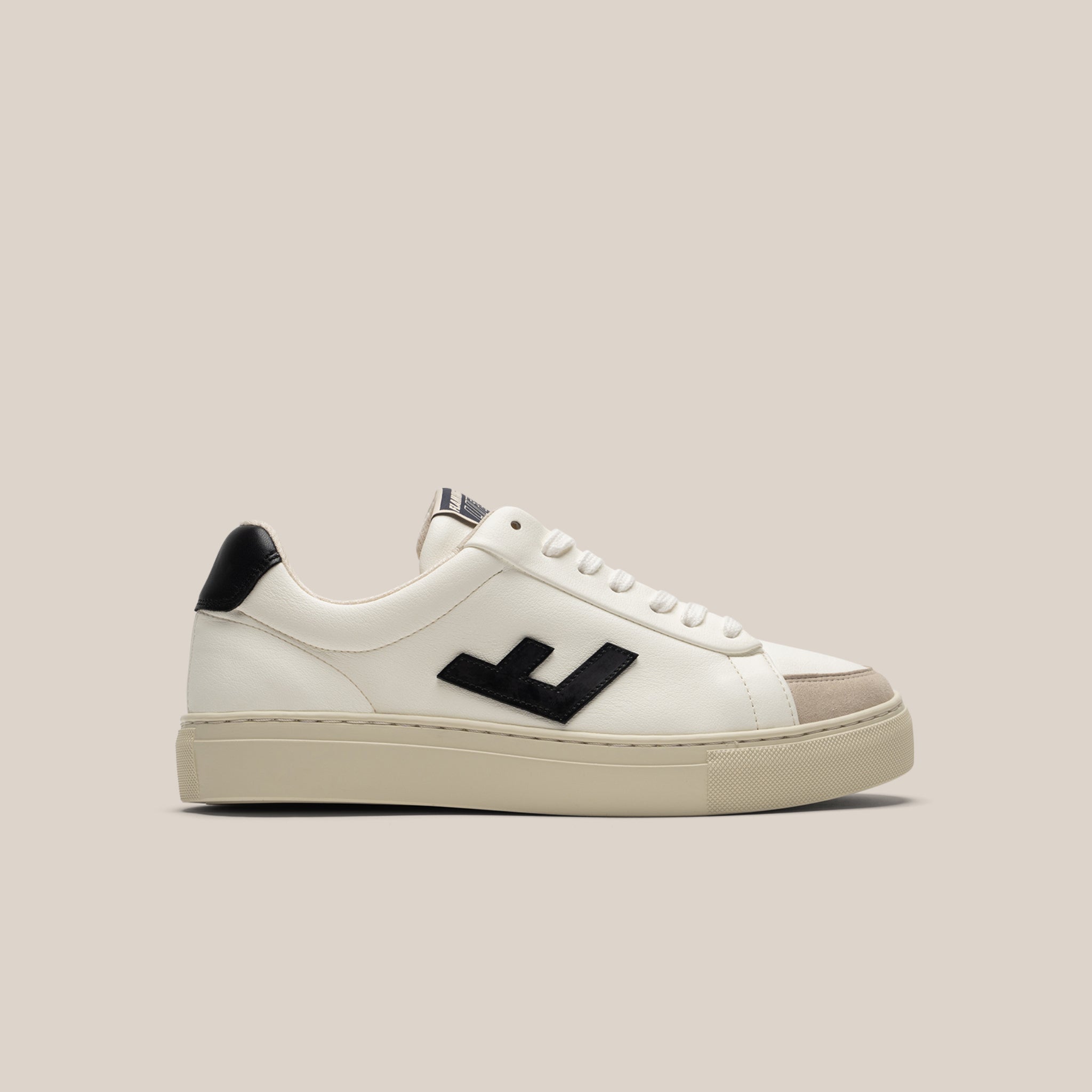 Weißer Sneaker mit schwarzem Akzent und hellem Sohlenrand auf beigem Hintergrund.