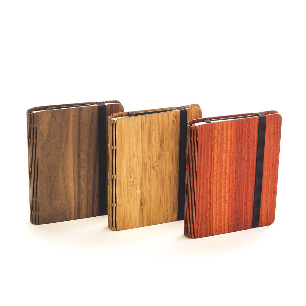 Drei Holznotizbücher in Braun, Hellbraun und Rot mit schwarzen Gummibändern stehen nebeneinander.