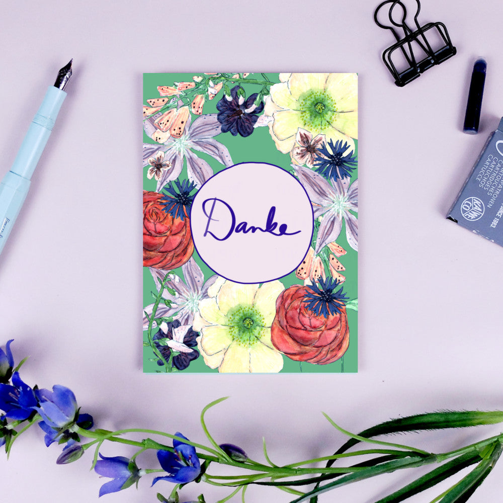 Eine Karte mit Blumenmuster und dem Wort "Danke" in der Mitte, umgeben von Büroklammern und einem Stift.