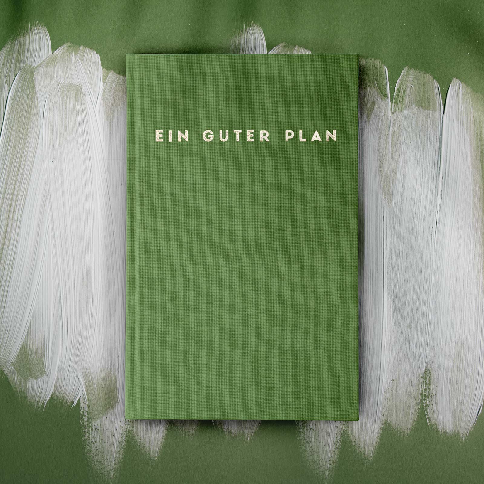 Ein grünes Buch mit der Aufschrift "EIN GUTER PLAN" auf einem mit weißer Farbe gestrichenen, grünen Hintergrund.