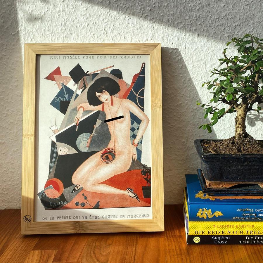 Gerahmte Grafik neben Bonsai auf Bücherstapel; Darstellung zeigt stilisierte, tänzerische Figur vor kubistischem Hintergrund.