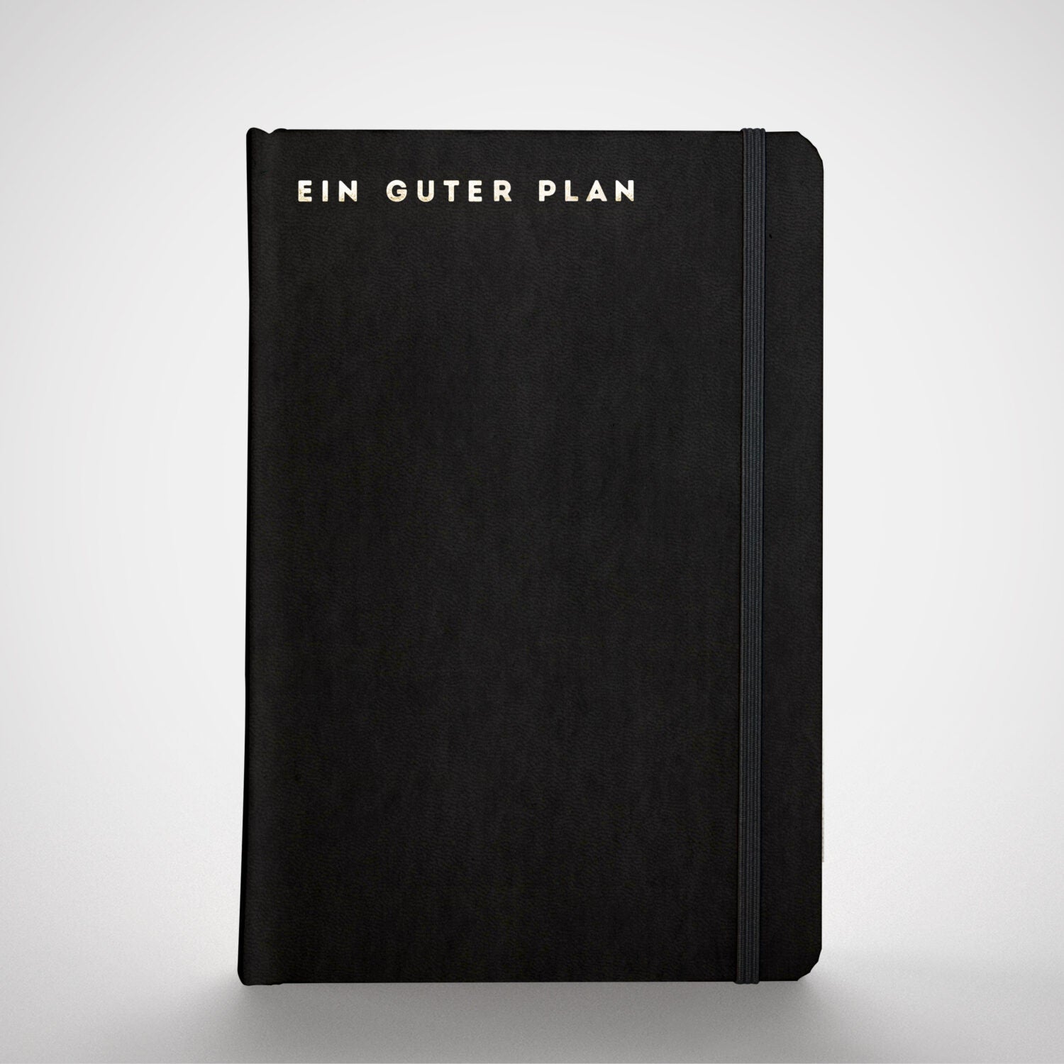 Schwarzes Notizbuch mit der Aufschrift "EIN GUTER PLAN" in weißen Buchstaben auf dem Einband, elastisch gebunden.