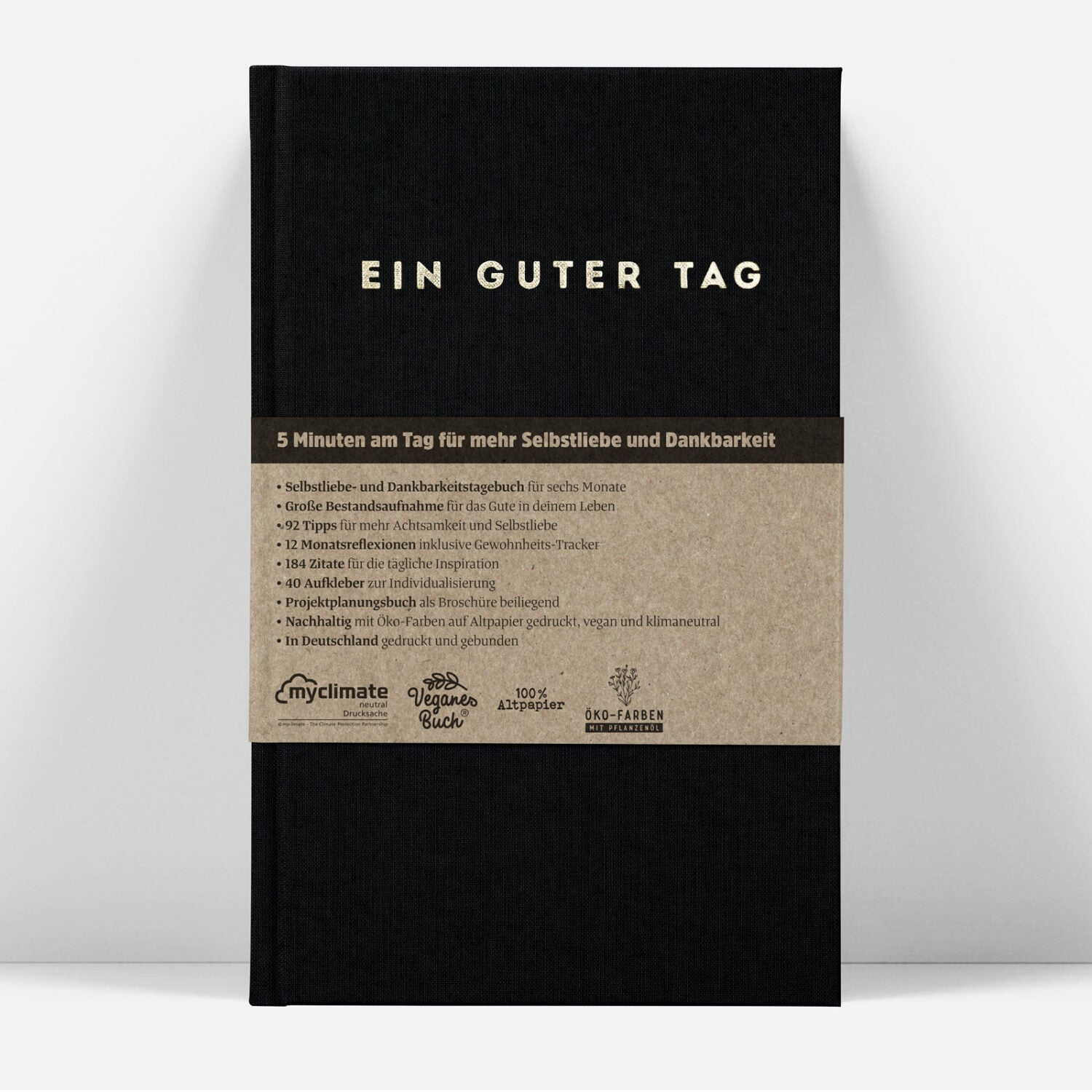 Schwarzes Tagebuch mit der Aufschrift "EIN GUTER TAG" und beige Details über Selbstliebe und Dankbarkeit.