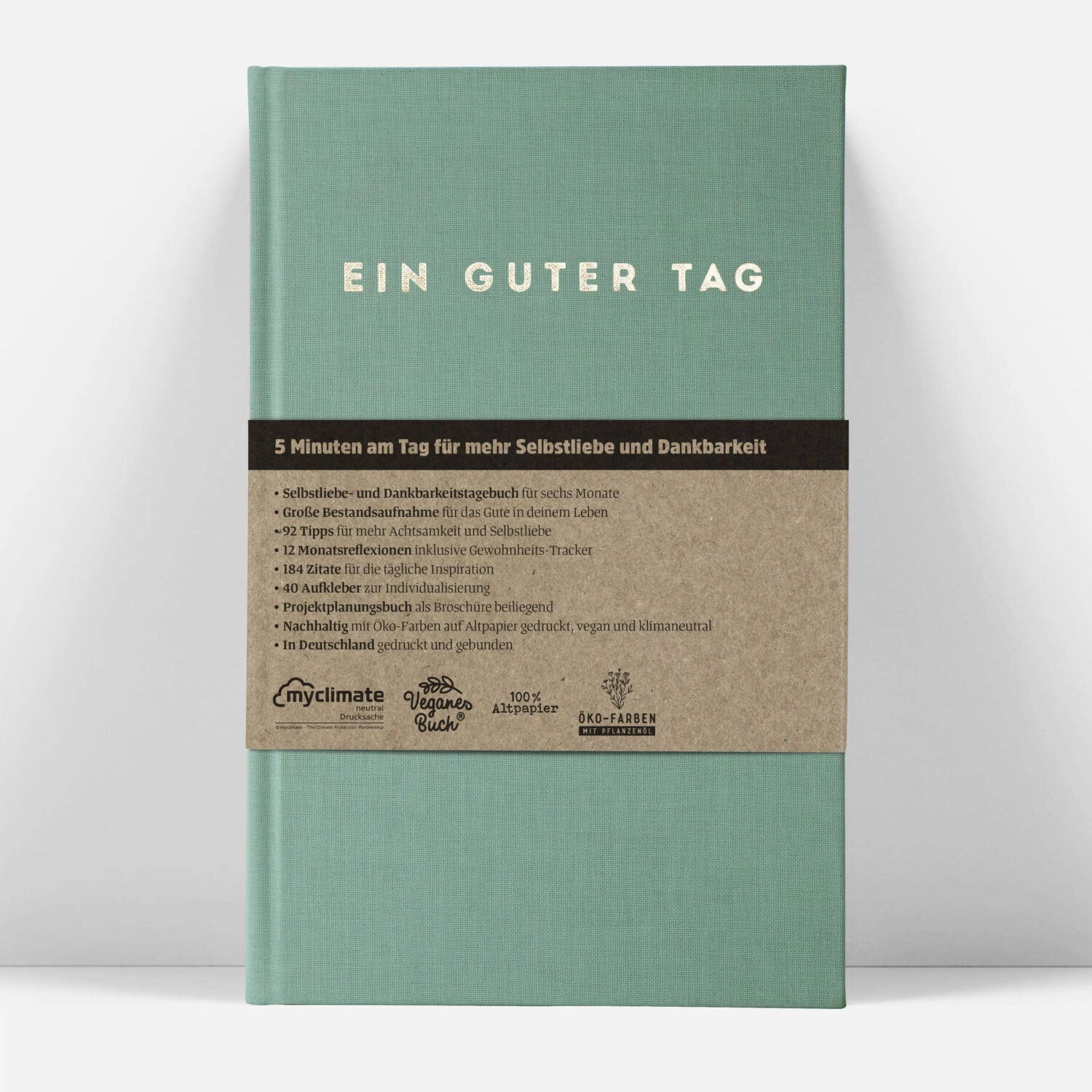 Grünes Buch mit dem Titel "Ein Guter Tag", Infos zu Selbstliebe und Nachhaltigkeit auf beigem Band darunter.