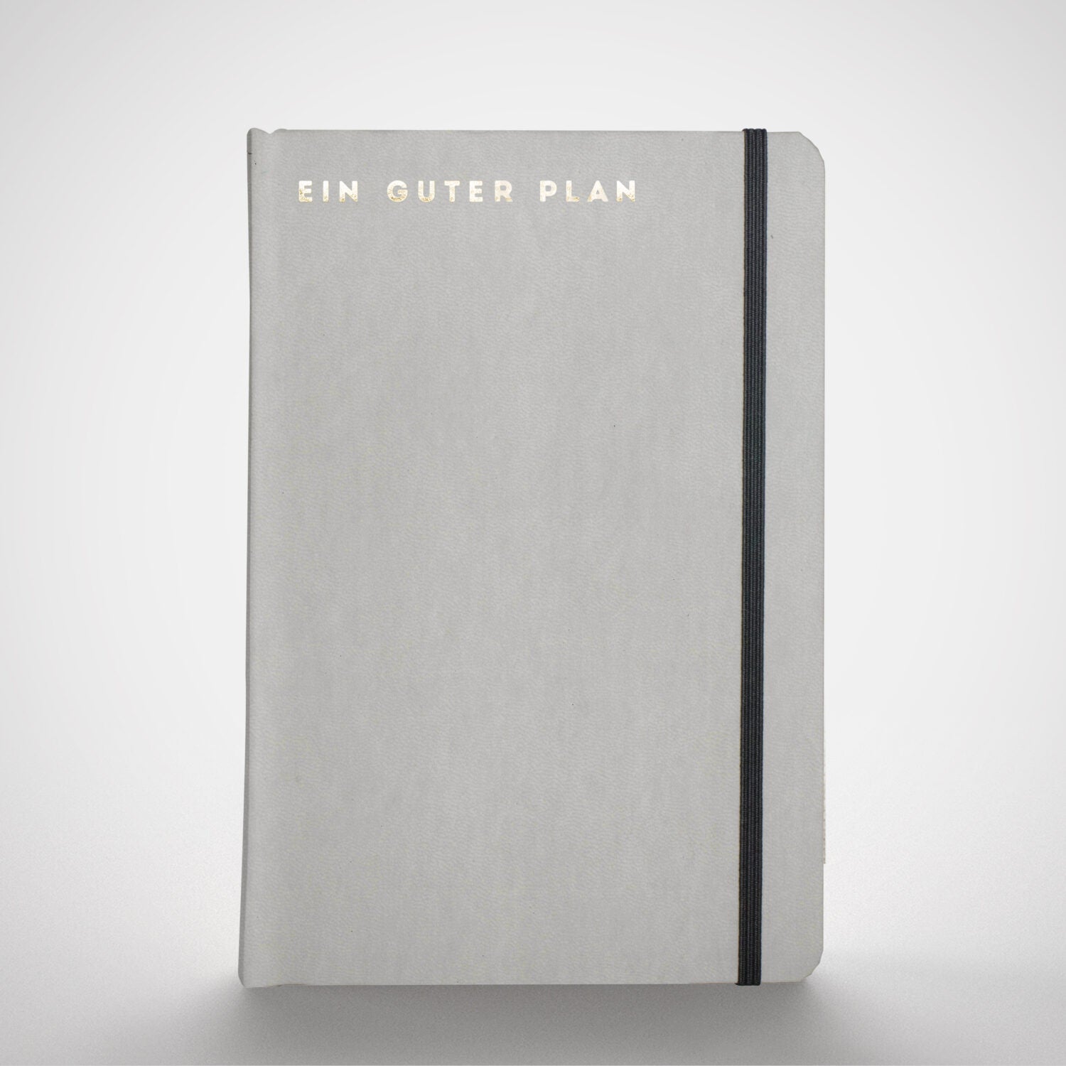 Graues Notizbuch mit der Aufschrift "EIN GUTER PLAN" in goldenen Buchstaben und einem schwarzen Gummiband.