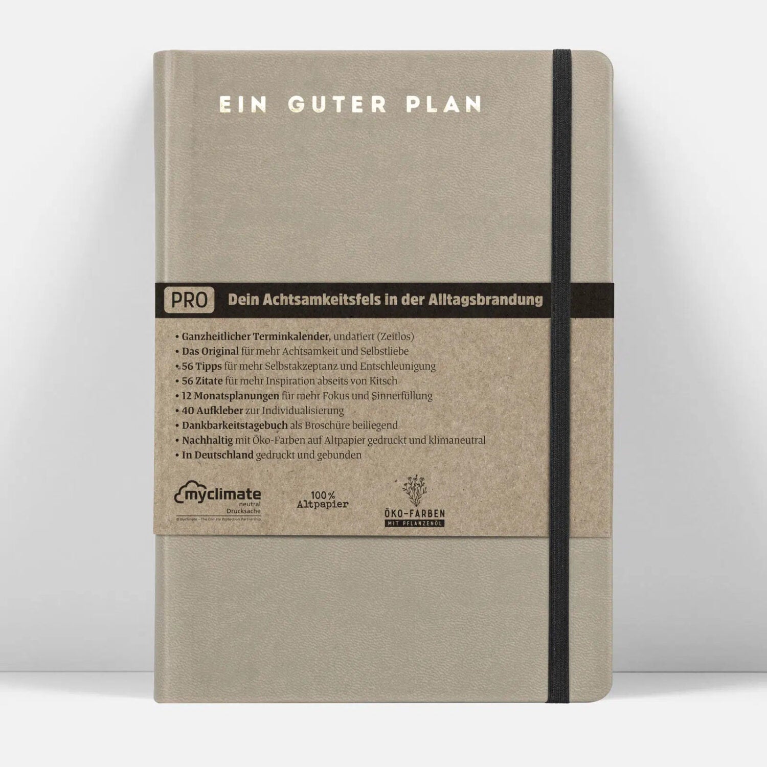 Graues Notizbuch mit der Aufschrift "EIN GUTER PLAN", schwarzem Gummiband und einer detaillierten Produktbeschreibung.