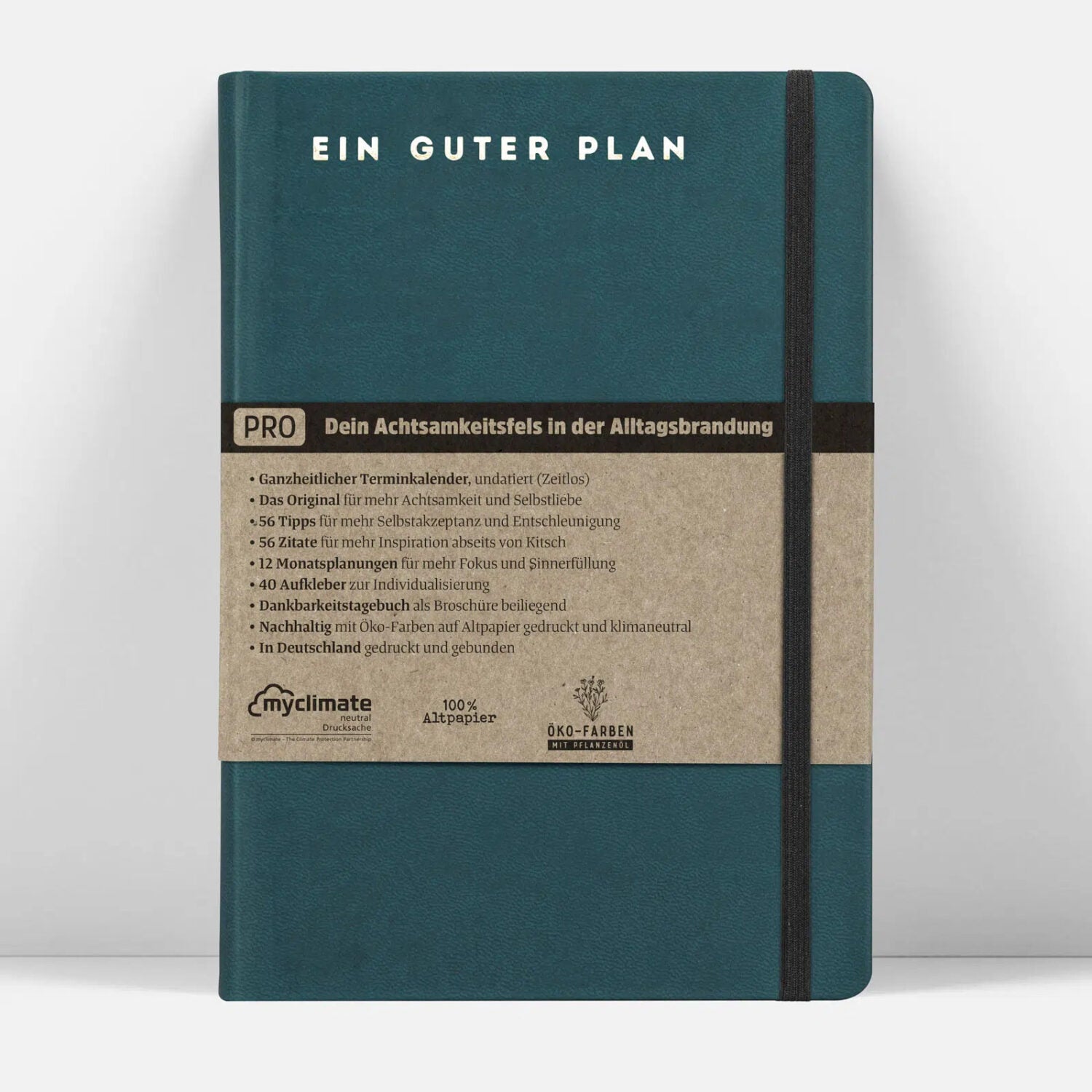 Grünes Notizbuch mit der Aufschrift "EIN GUTER PLAN" und einem braunen Papierband mit Details zur Nachhaltigkeit.