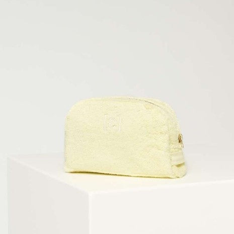 Gelbes, strukturiertes Kosmetiketui auf einem weißen Podest vor einem neutralen Hintergrund.