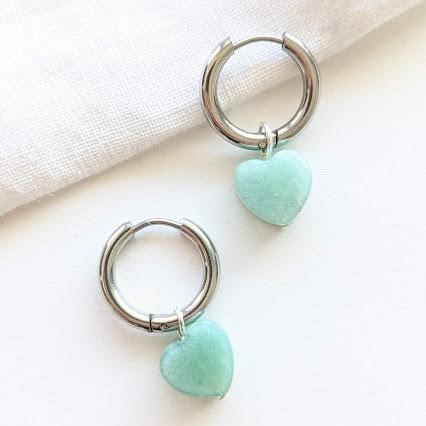 Silberne Creolen mit türkisfarbenen Herzanhängern auf weißem Hintergrund.