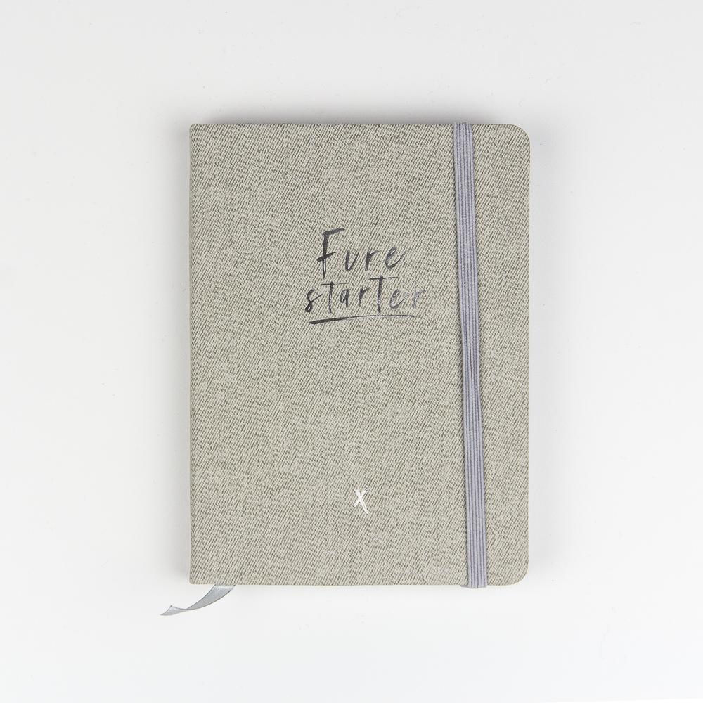 Graues Notizbuch mit dem Text "Firestarter" auf dem Cover, gesichert mit einem elastischen Band.