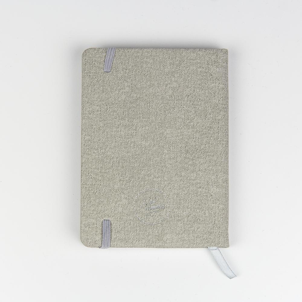Graues Notizbuch mit Stoffeinband, elastischem Band und Lesezeichen, flach auf weißem Hintergrund liegend.