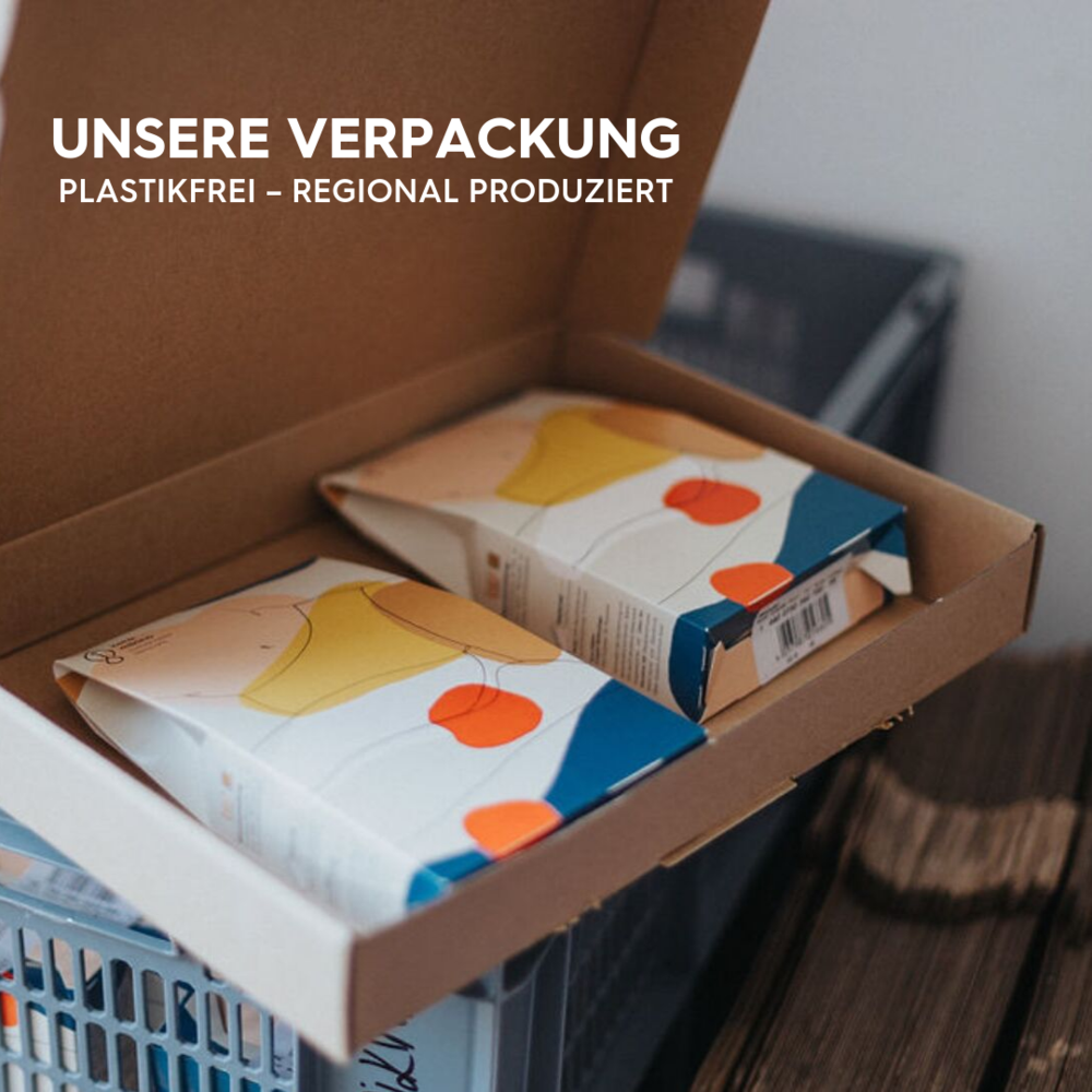 Offene Verpackung mit zwei bunt gestalteten Schachteln, darüber Text zu plastikfreier und regionaler Produktion.