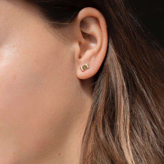 Nahaufnahme eines Ohres mit einem kleinen goldenen rechteckigen Ohrring.
