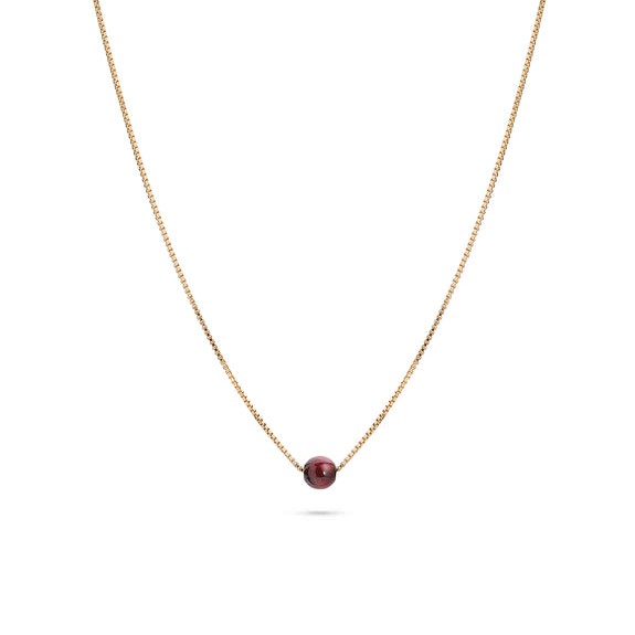 Goldene Halskette mit einer einzelnen, dunkelroten Perle in der Mitte.