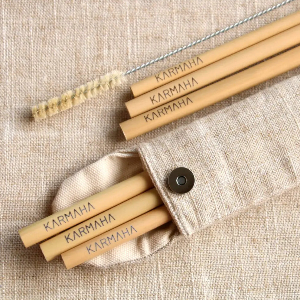 Mehrere Bambus-Strohhalme mit der Aufschrift "Karmaha" liegen neben einer Bürste und einem Stoffetui auf Leinenstoff.