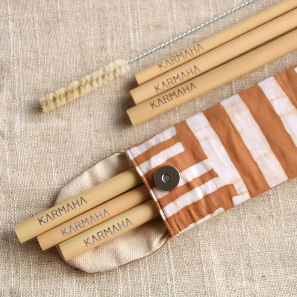 Bambus-Trinkhalme mit Reinigungsbürste und gestreiftem Stoffetui auf einem beigen Untergrund.