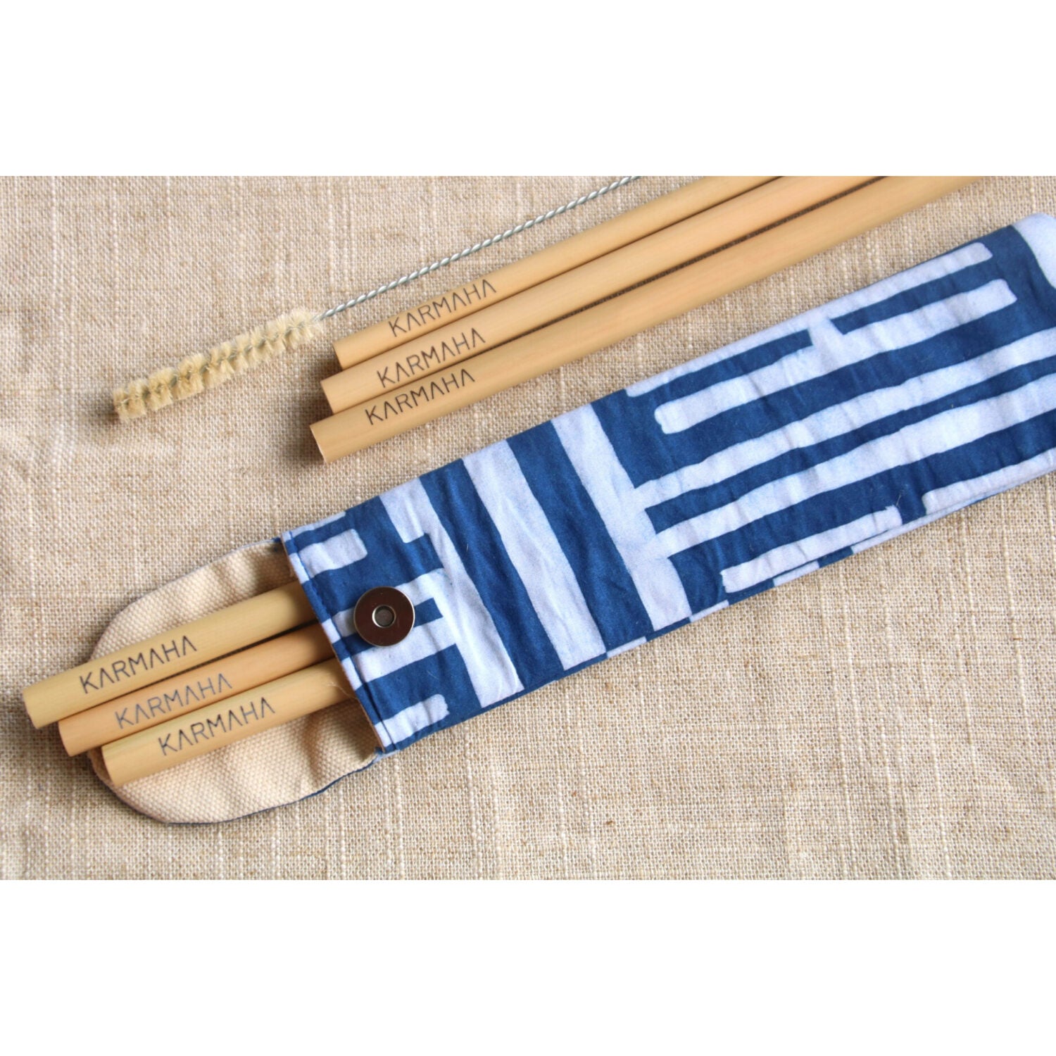 Ein Set aus Bambusstrohhalmen und einer Reinigungsbürste liegt neben einem blau-weiß gemusterten Stoffetui auf beigem Stoff.