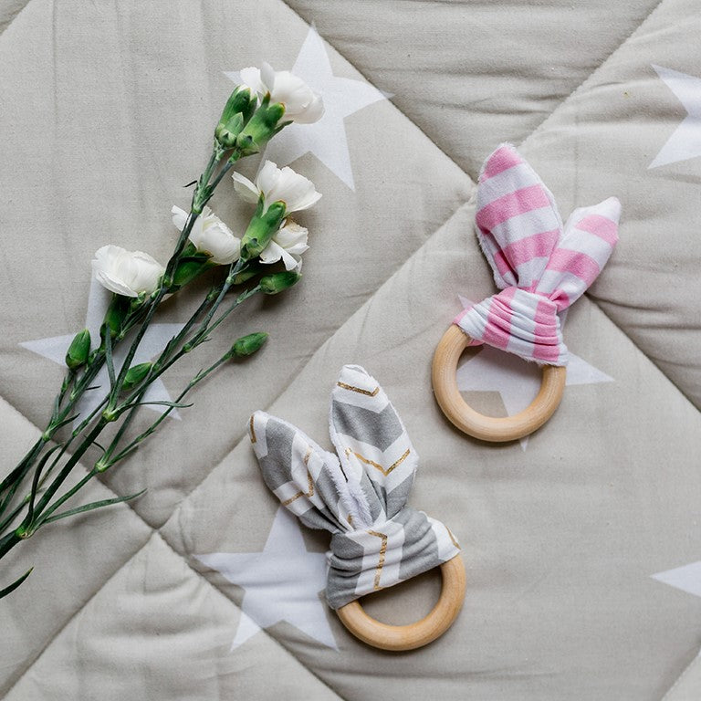 Zwei Holzrasseln mit Stoffohren neben weißen Nelken auf einer grauen Decke mit weißen Sternen.